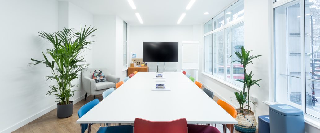 Modern meeting room with large white table and colorful chairs for workshops and team meetings.