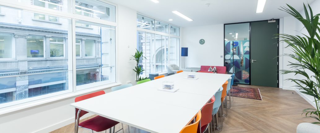 Modern meeting space in Covent Garden with large white table and colorful chairs.