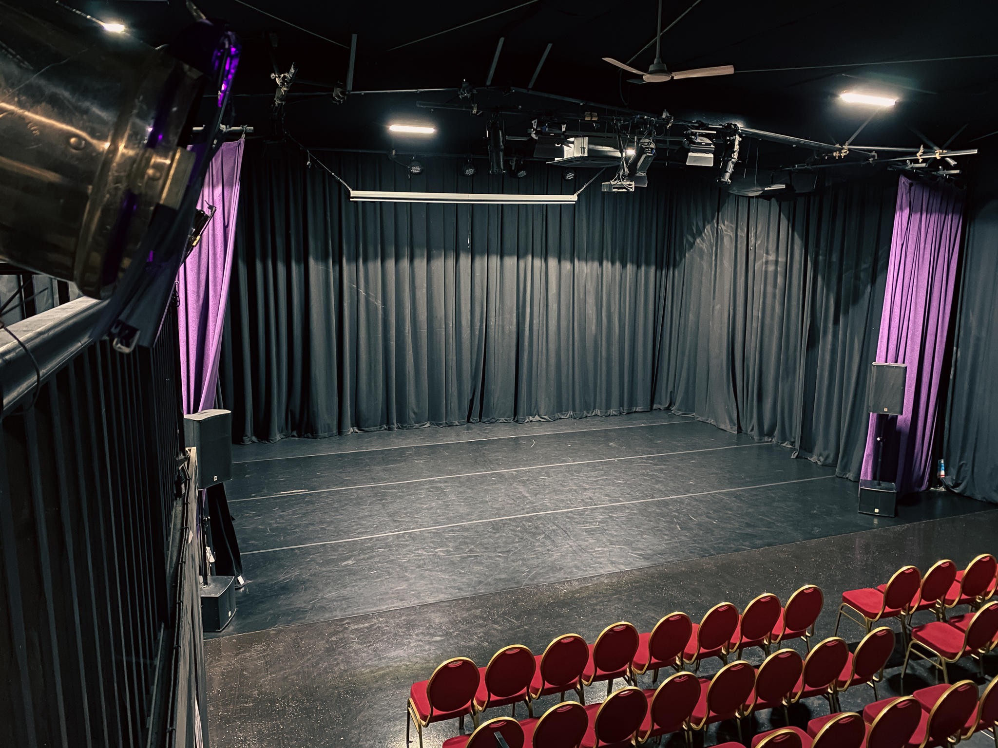 Versatile event space with black stage and purple drapes for presentations and performances.