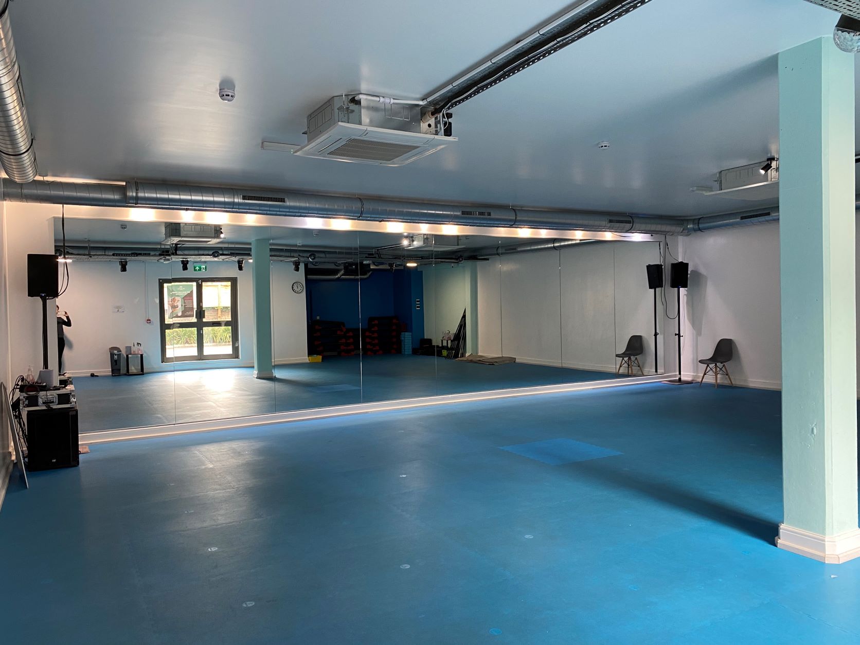 Versatile gym space with mirrors and blue flooring for workshops and fitness classes.