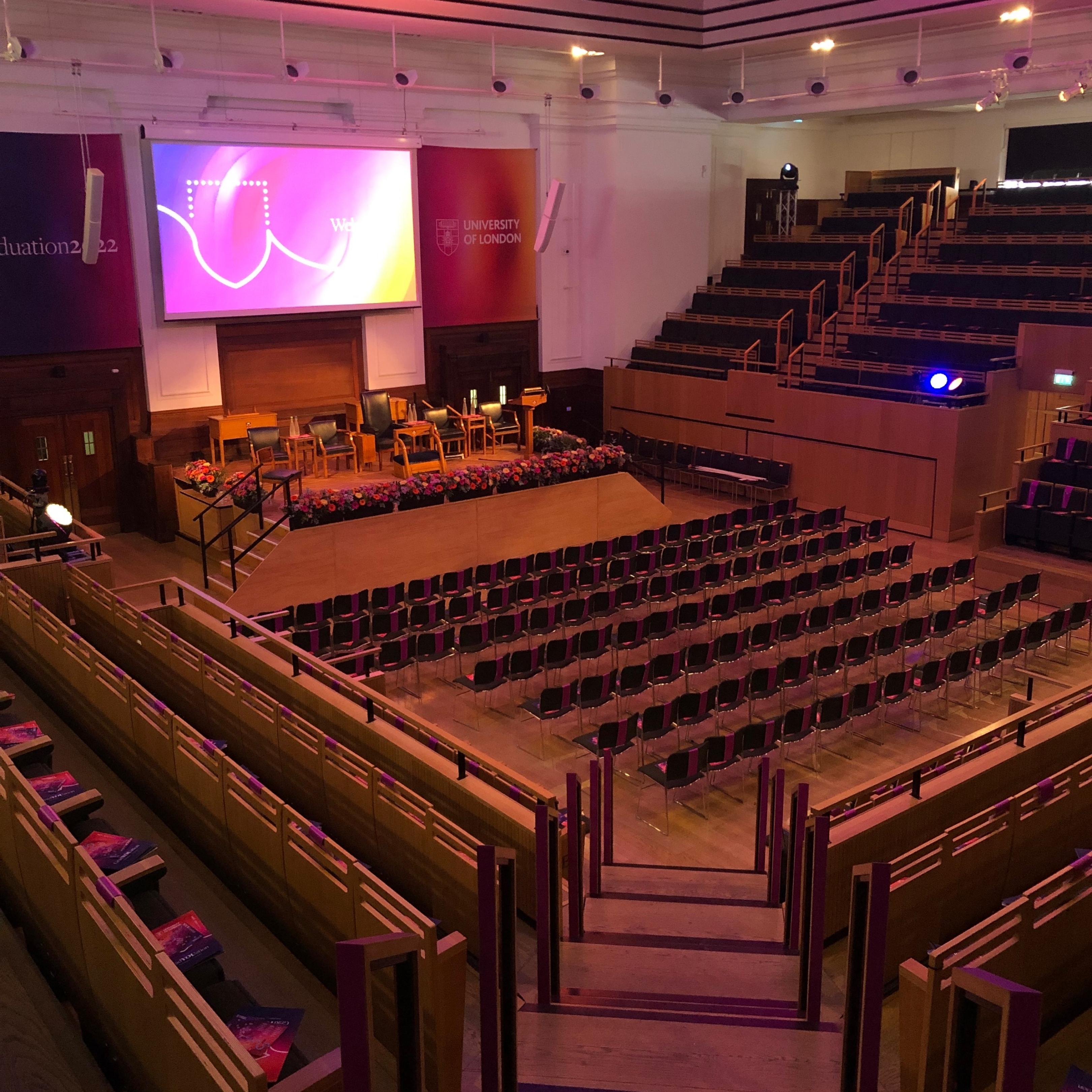 Event space with stage and seating for conferences, featuring elegant floral arrangements.