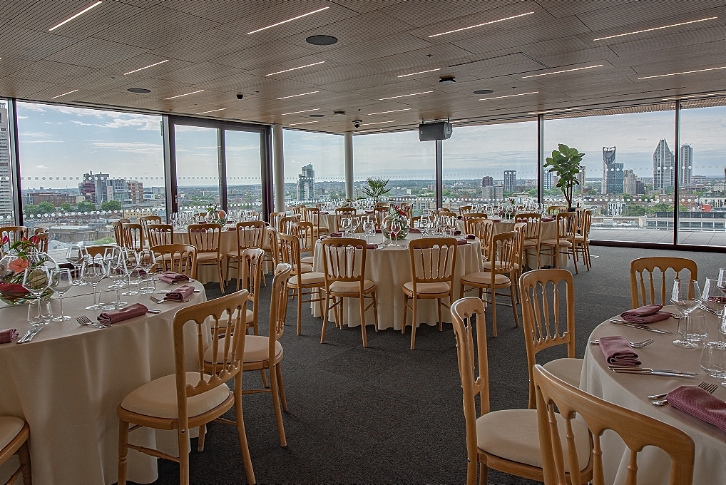 Sophisticated event space with floral centerpieces and skyline view for weddings or corporate events.