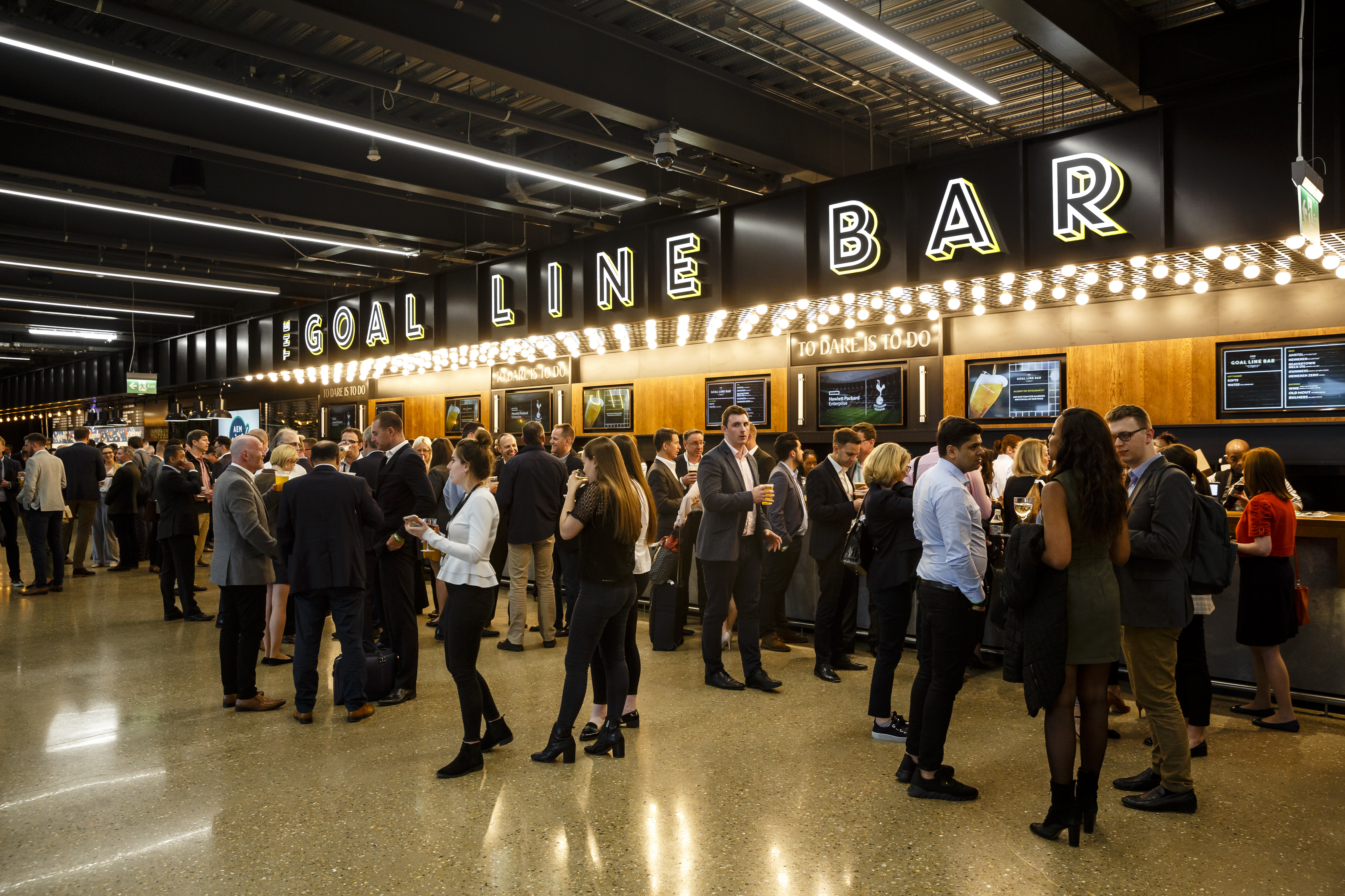Vibrant networking event at Tottenham Hotspur Stadium with stylish bar and lively atmosphere.