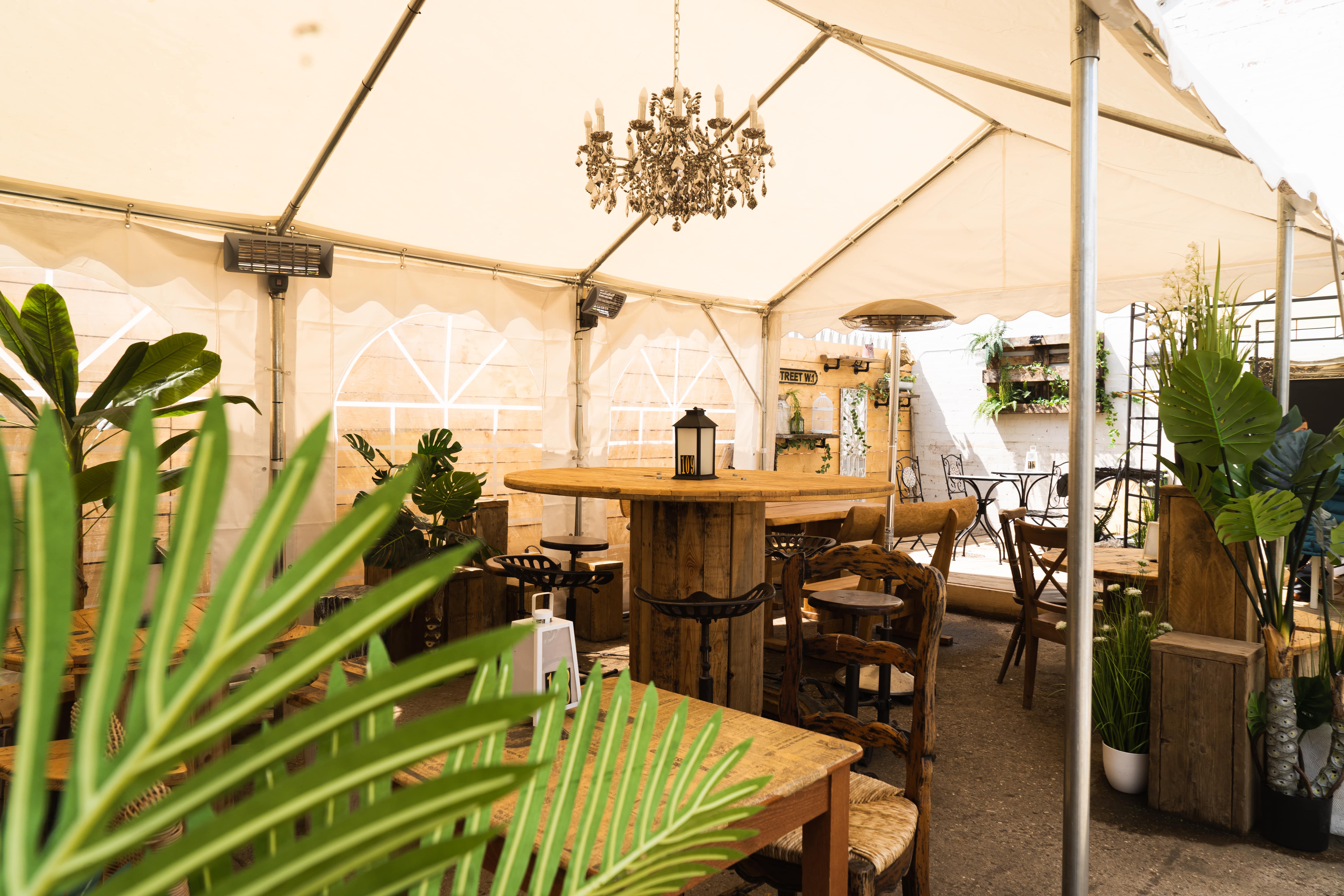 Elegant tented event space with rustic furniture and chandelier for intimate gatherings.