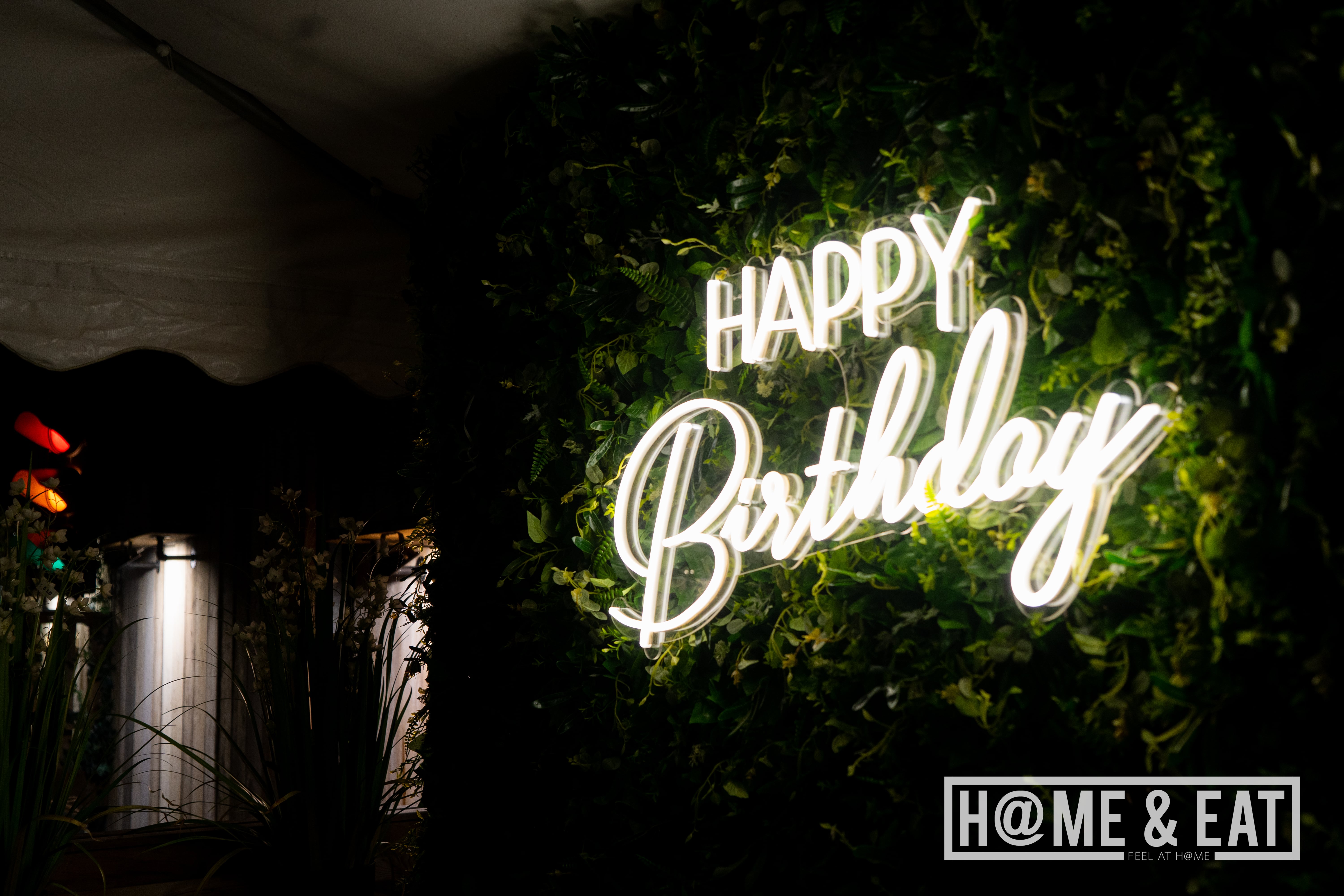 Vibrant birthday backdrop with neon sign and lush greenery for event celebrations.