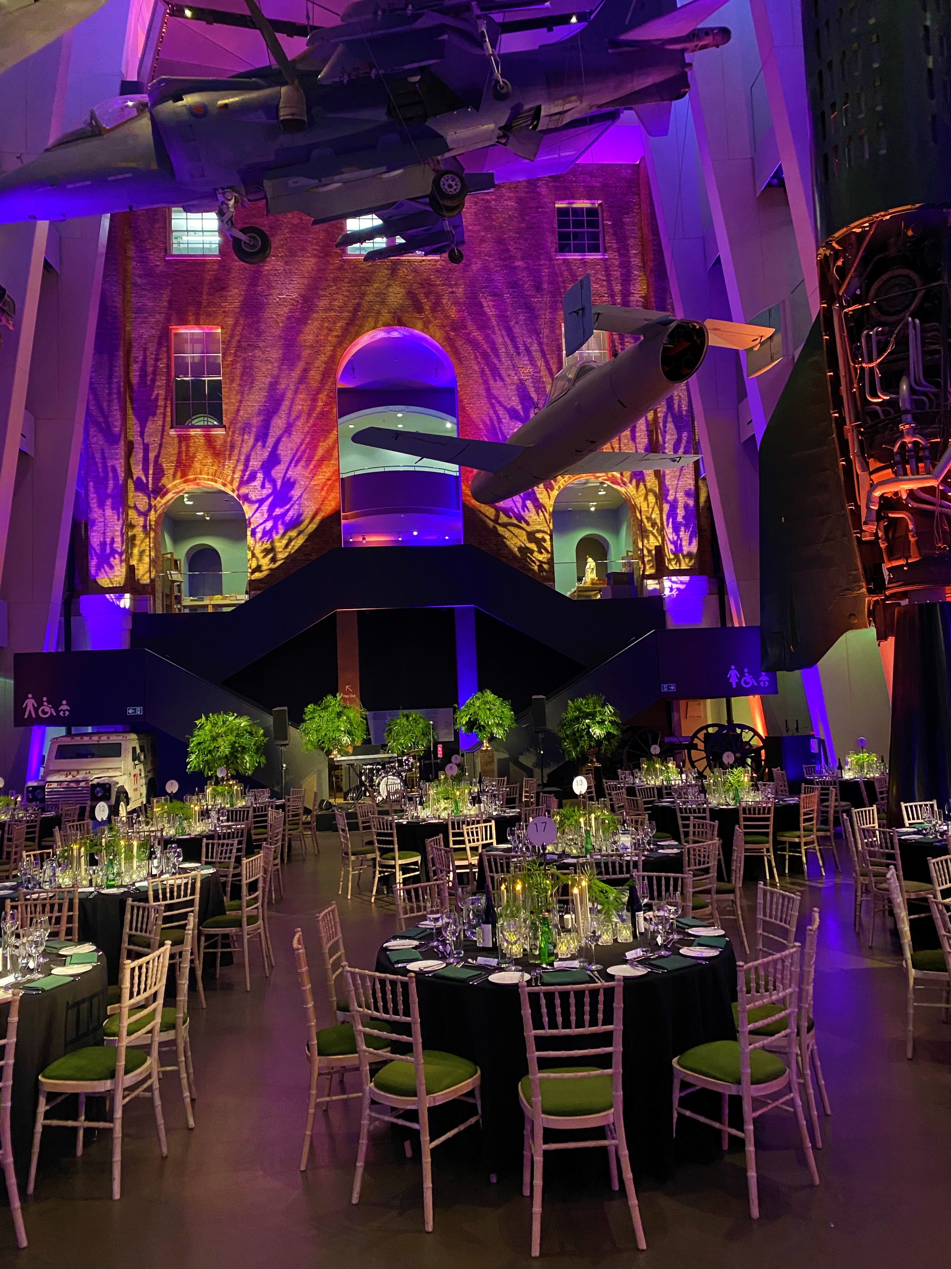 Atrium at IWM London with elegant tables and suspended aircraft for corporate events.