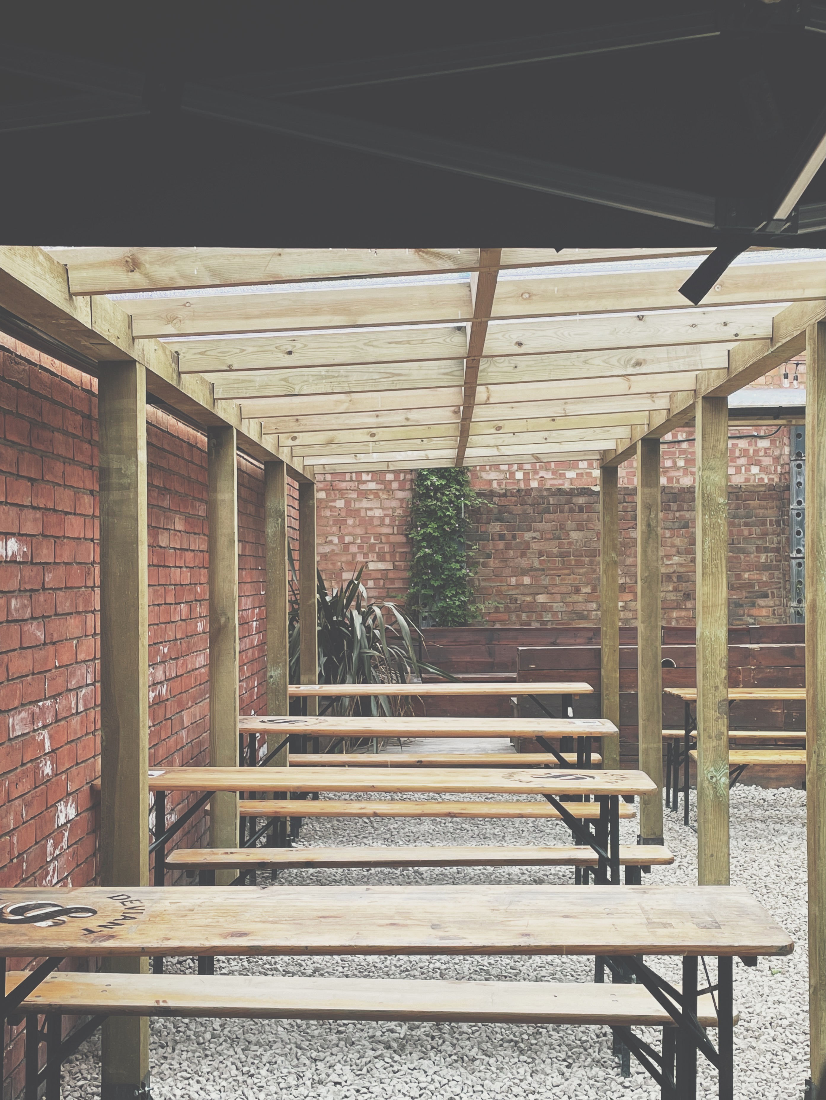 Outdoor event space at Deviant & Dandy Brewery with wooden pergola and greenery.