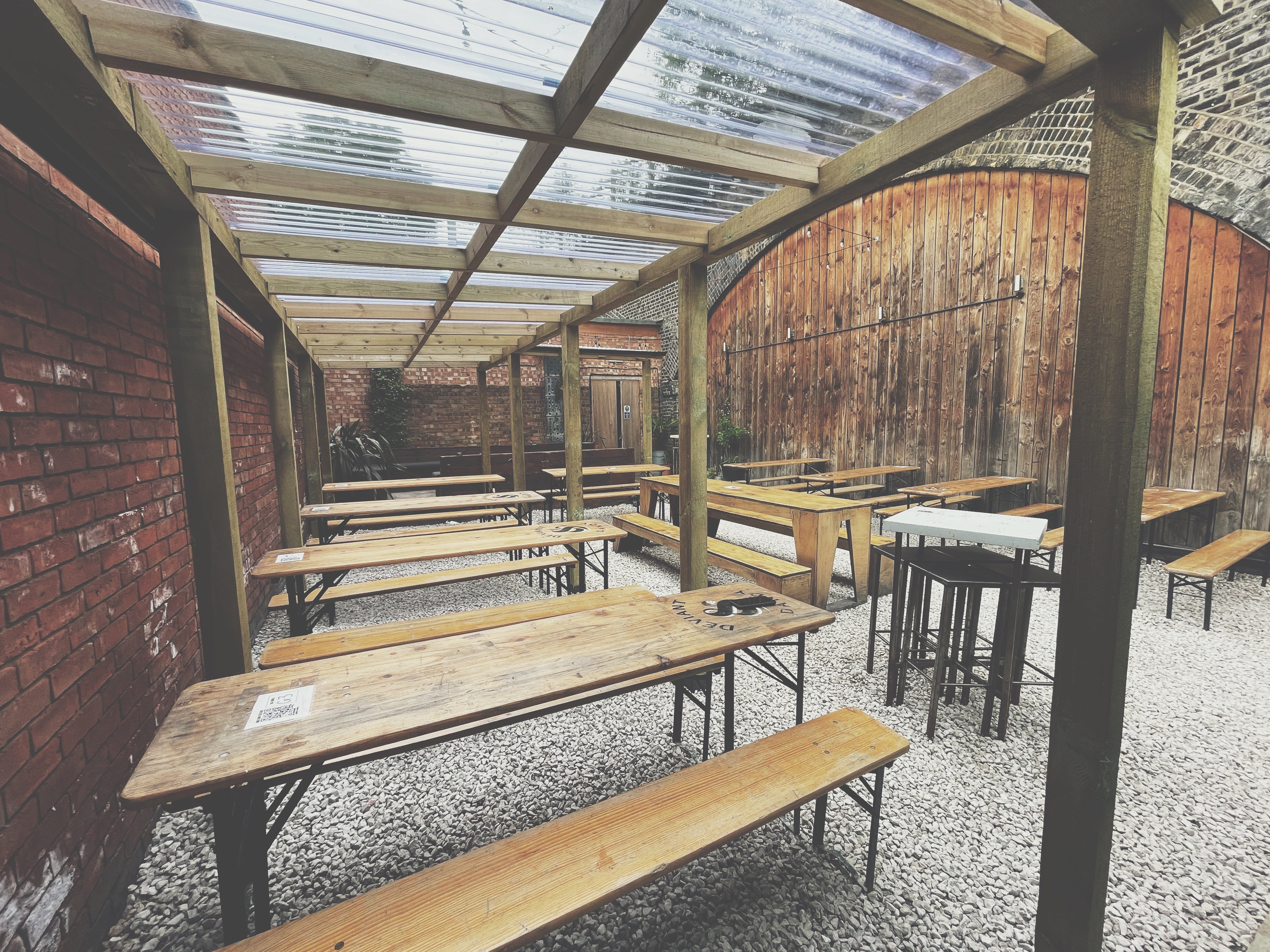Outdoor event space at Deviant & Dandy Brewery with rustic wooden tables and high-tops.