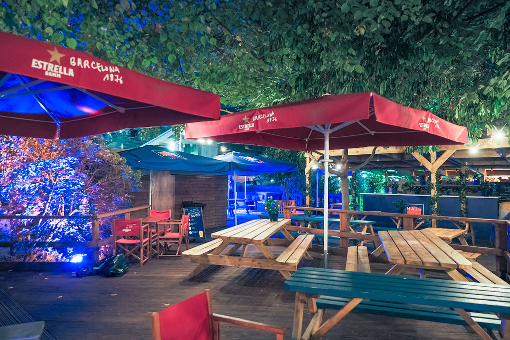 Vibrant outdoor event space with picnic tables and red umbrellas for casual gatherings.