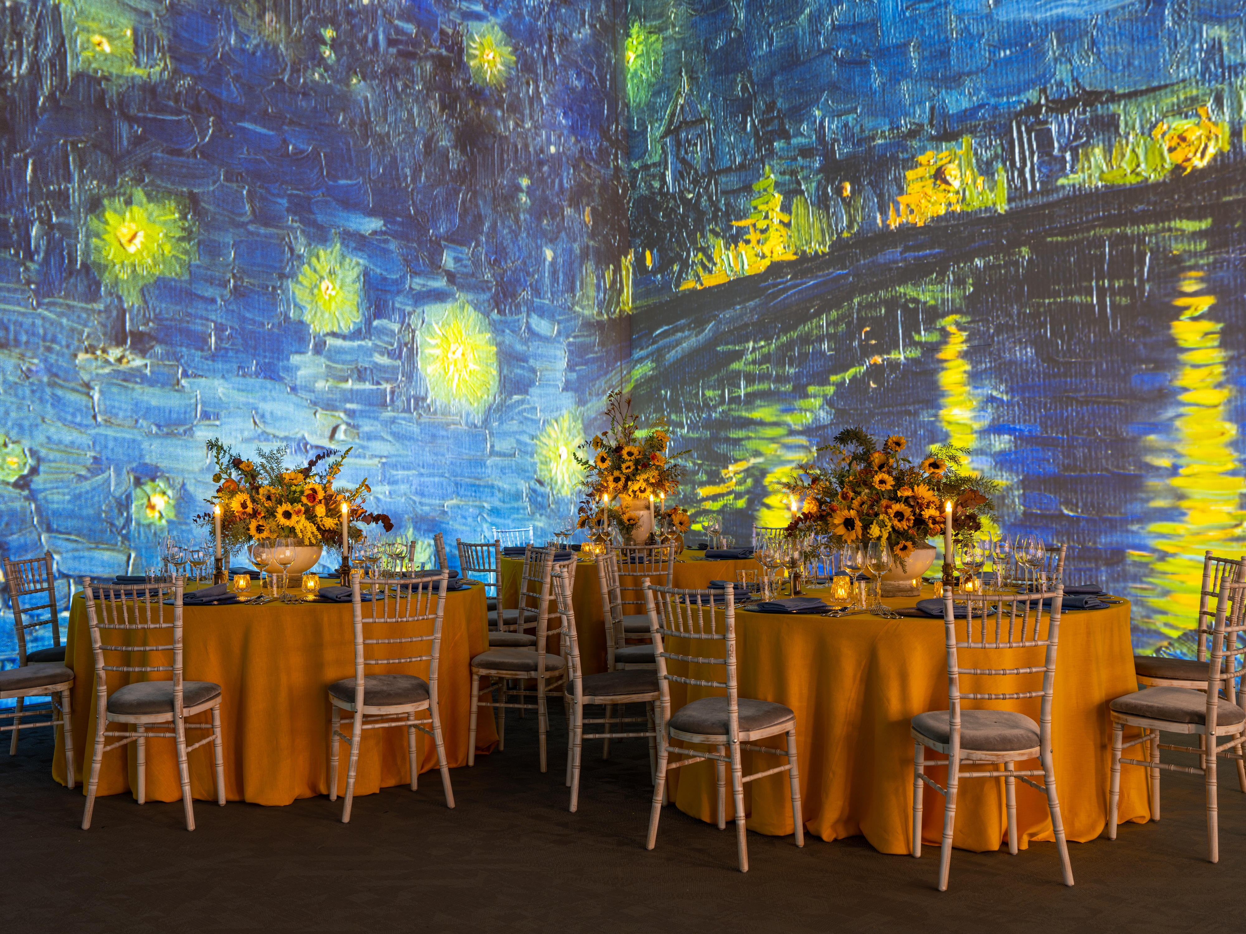 Elegant event space with yellow tables and Van Gogh projection for upscale gatherings.