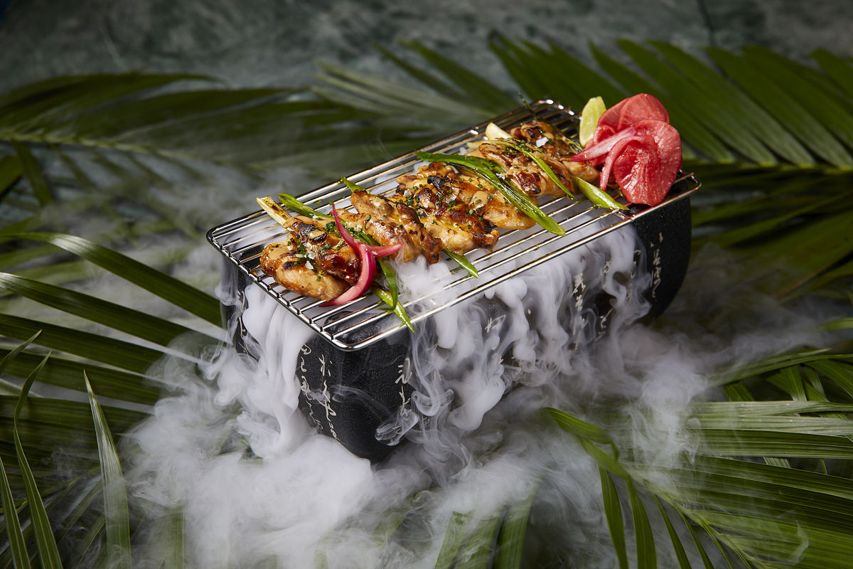 Grilled skewers on a smoky grill amidst tropical foliage for outdoor events.