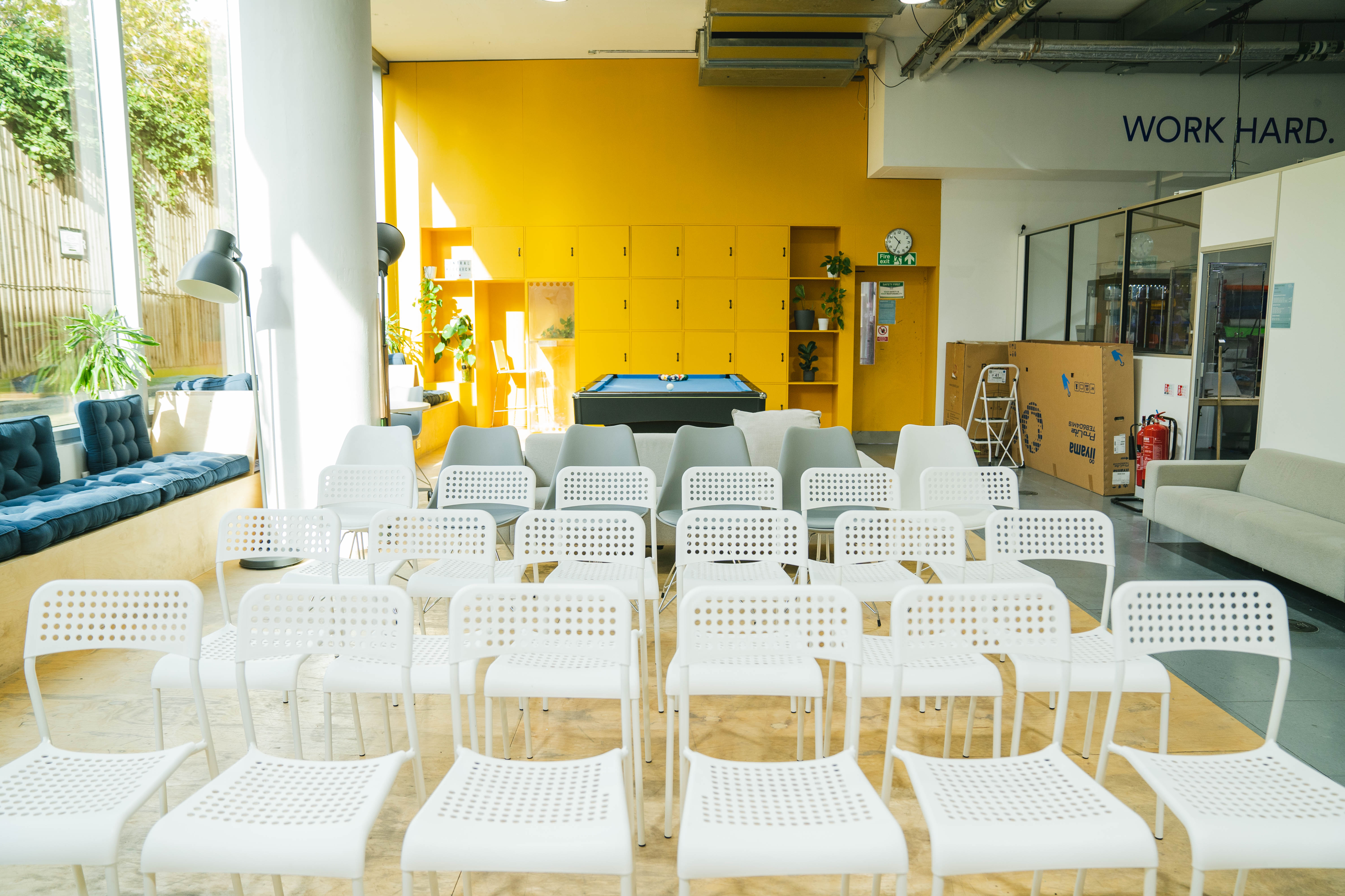 Modern event space with white chairs and yellow accent wall, perfect for meetings and networking.