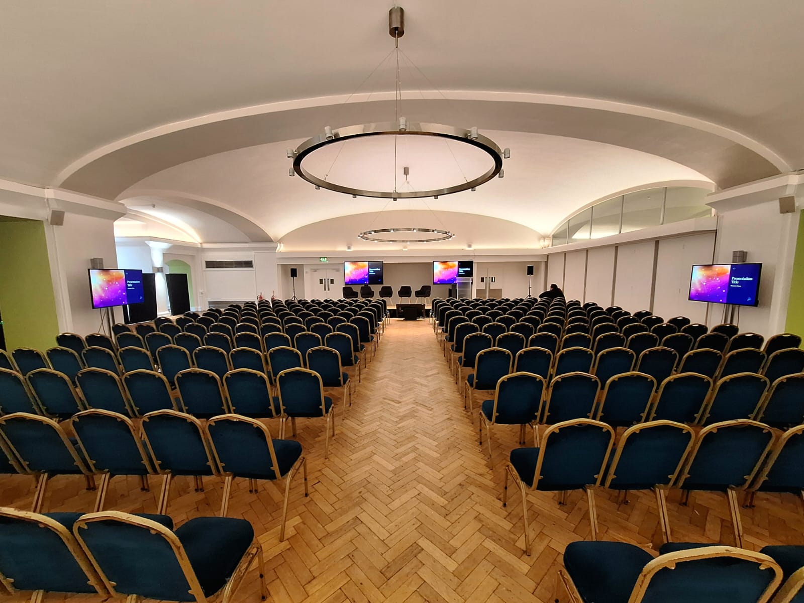 Conference room at Aldersgate, featuring blue chairs and dual screens for seminars.