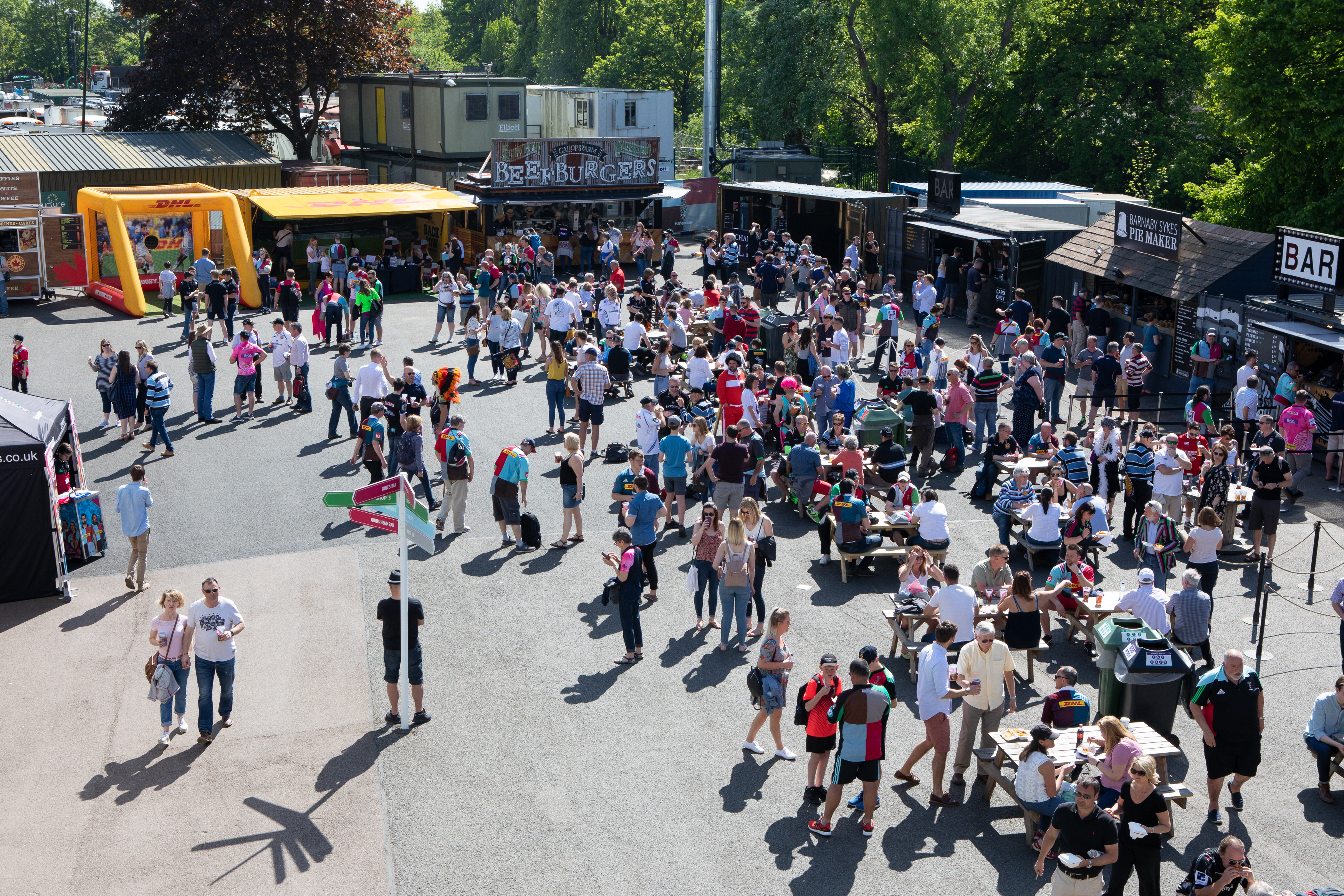 Vibrant outdoor event at Twickenham Stoop Stadium with food stalls and socializing.