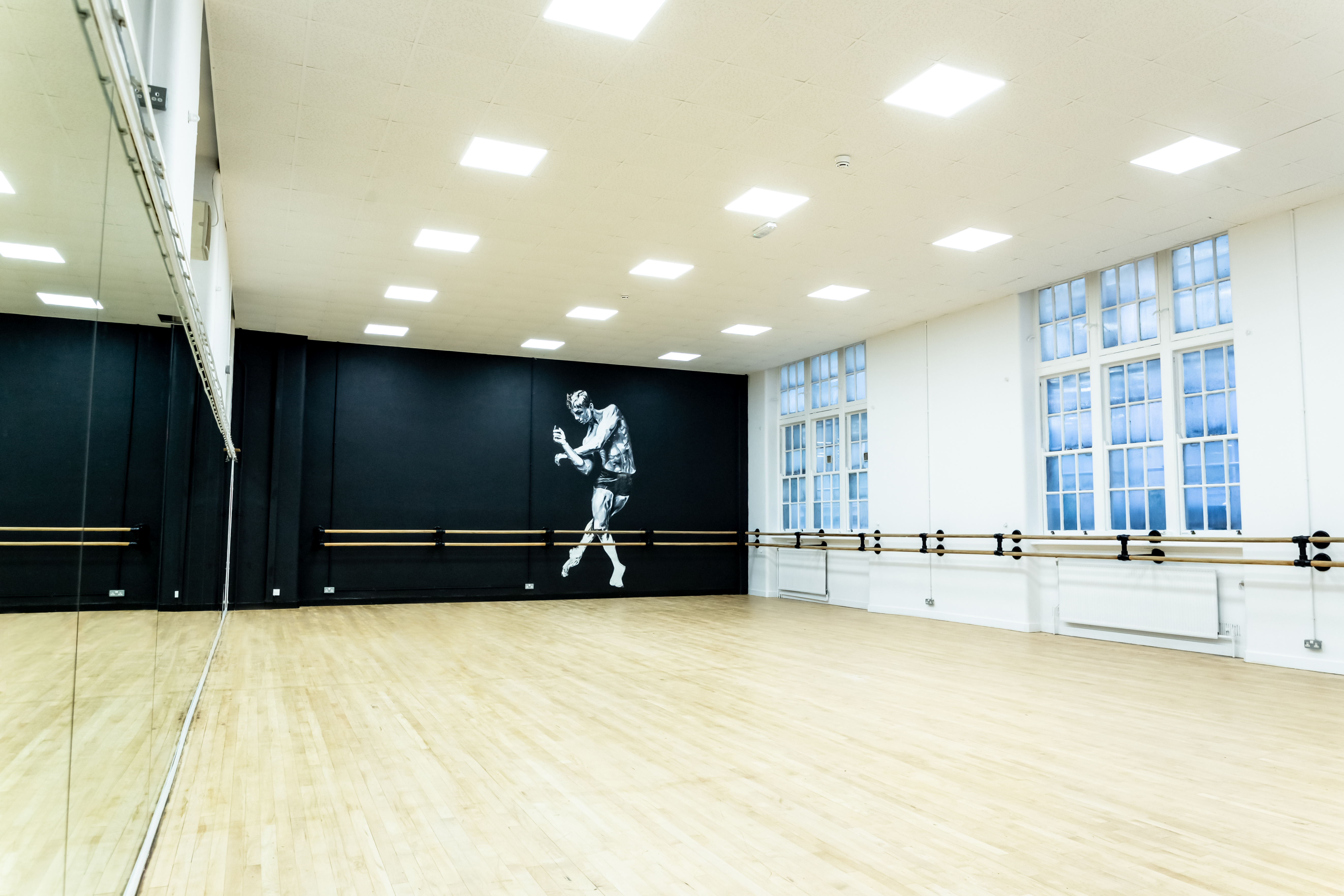 Spacious dance studio with wooden floor and mural, ideal for workshops and events.