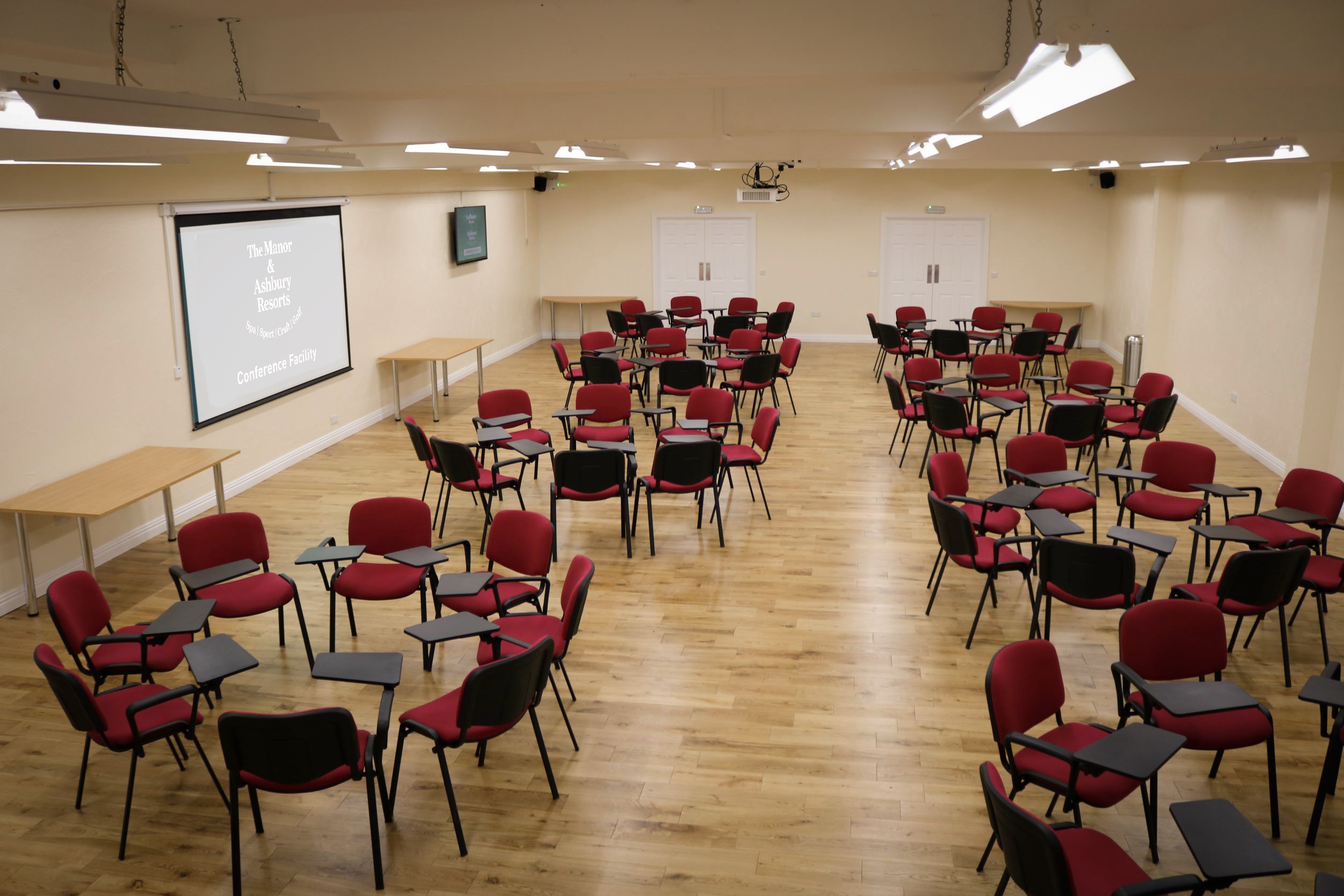 Versatile workshop space with red chairs and projector screen at Manor & Ashbury Resorts.