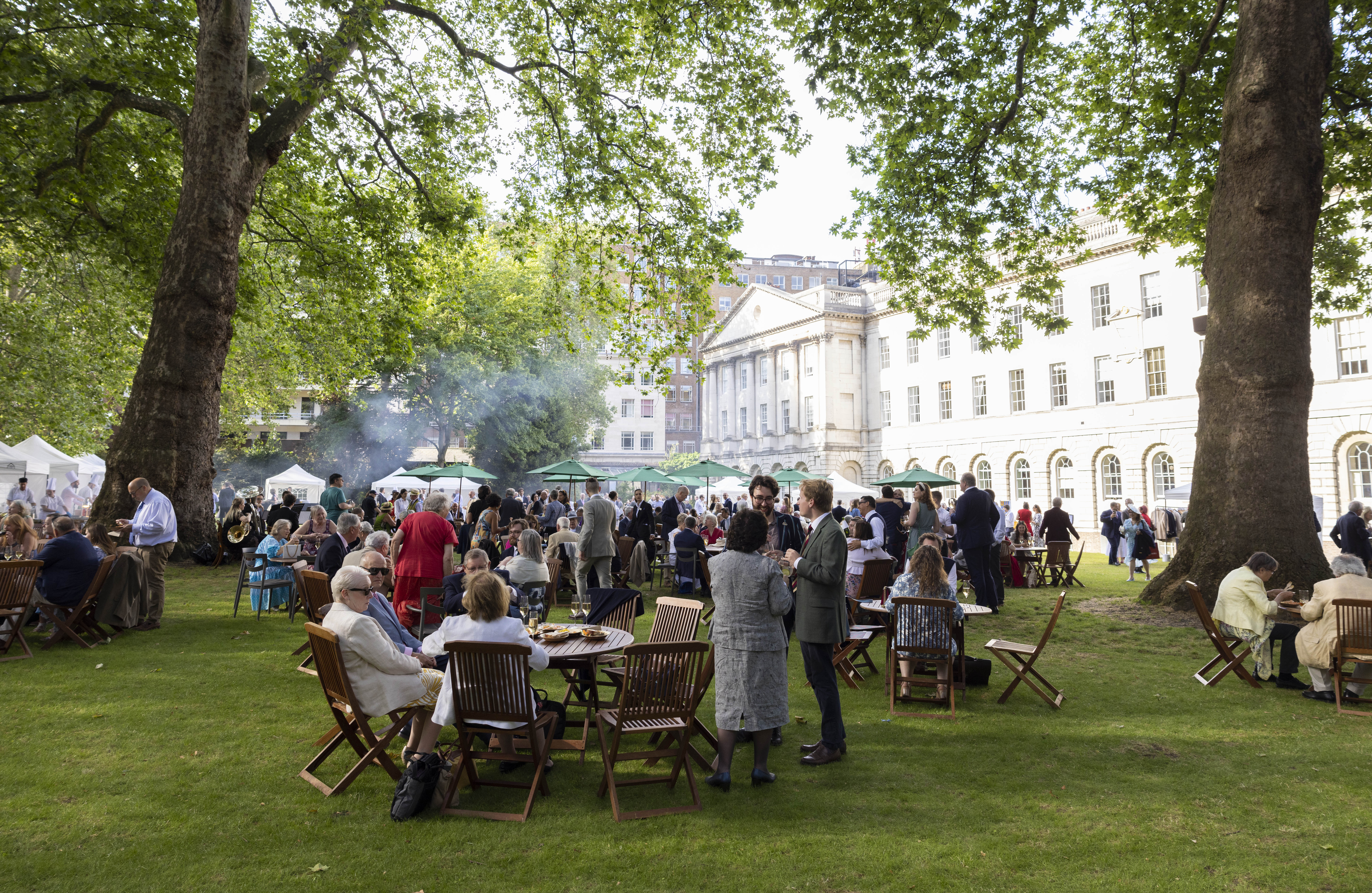Summer networking event on North Lawn, featuring attendees under large trees.