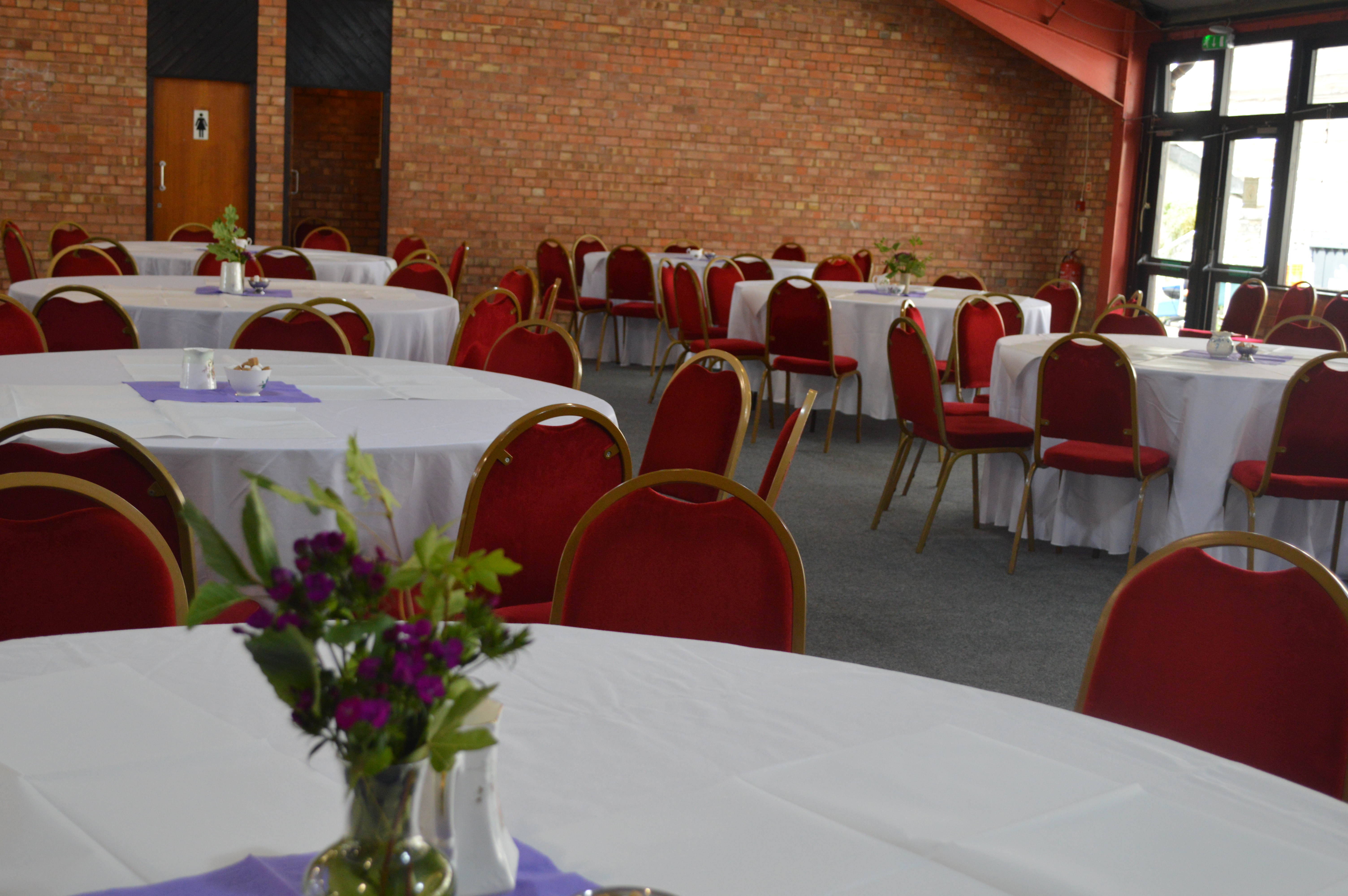 Montgomeryshire Pavilion event space with round tables and red chairs for gatherings.
