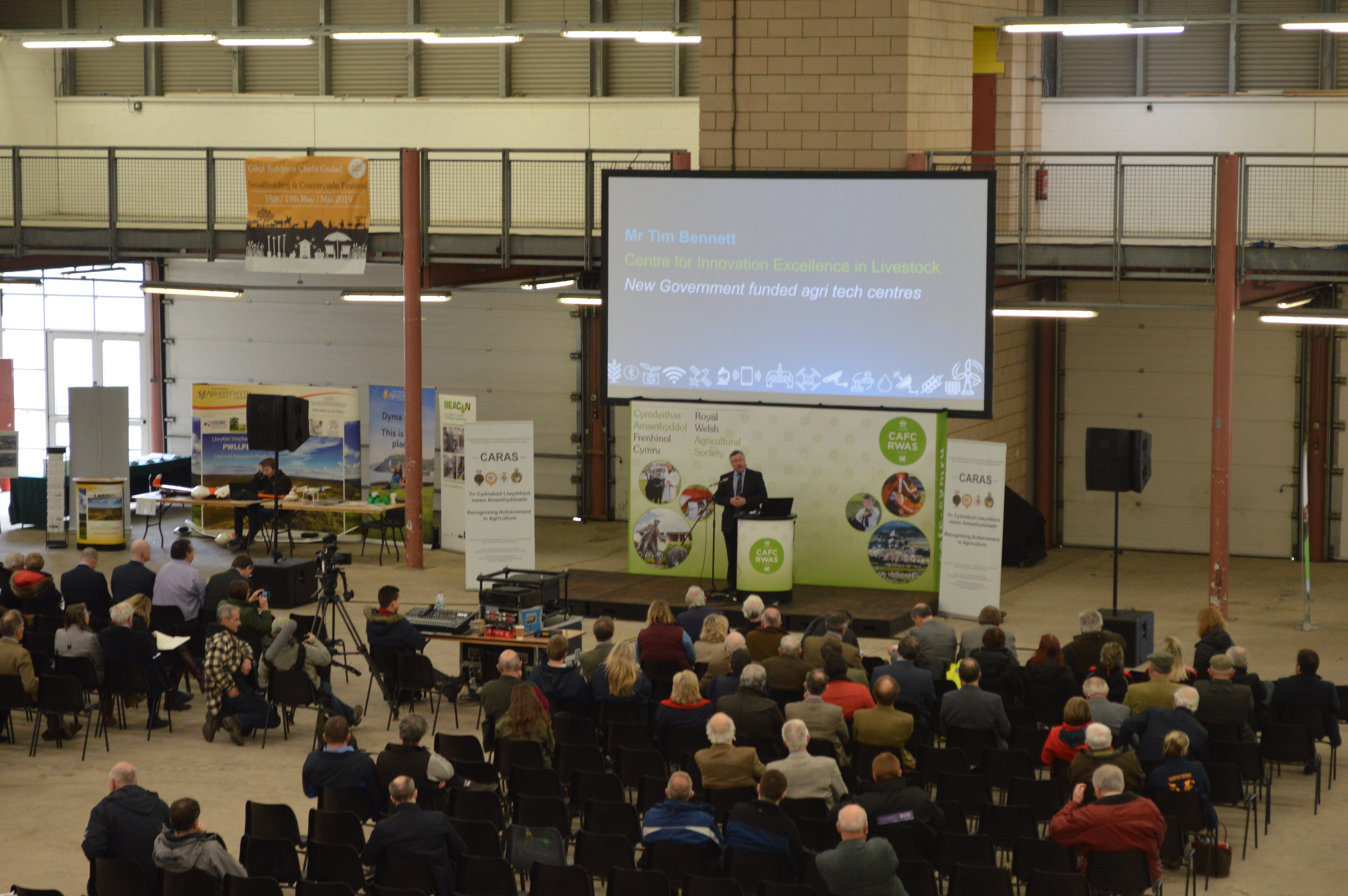 Exhibition Hall at Royal Welsh Showground with speaker addressing engaged audience, event space.