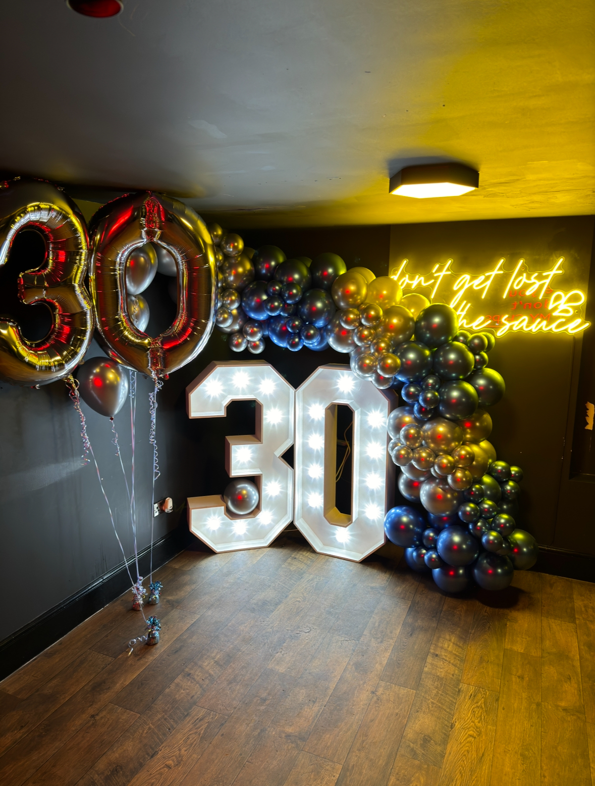 "30th birthday celebration with illuminated numbers and dark balloon arch backdrop"