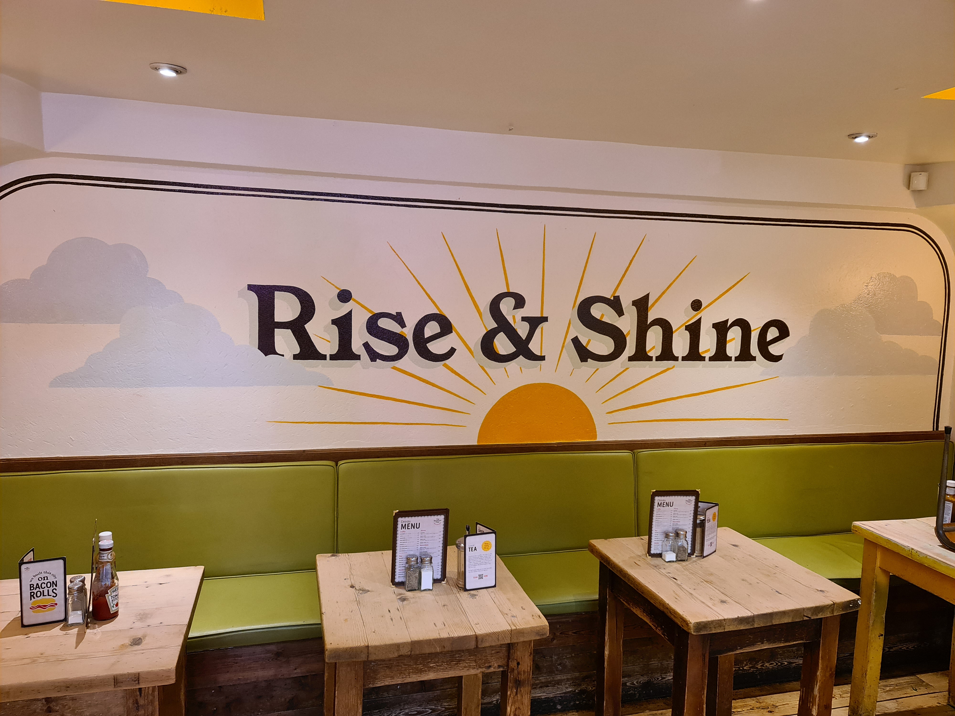 Vibrant café with "Rise & Shine" mural, ideal for morning meetings and networking events.