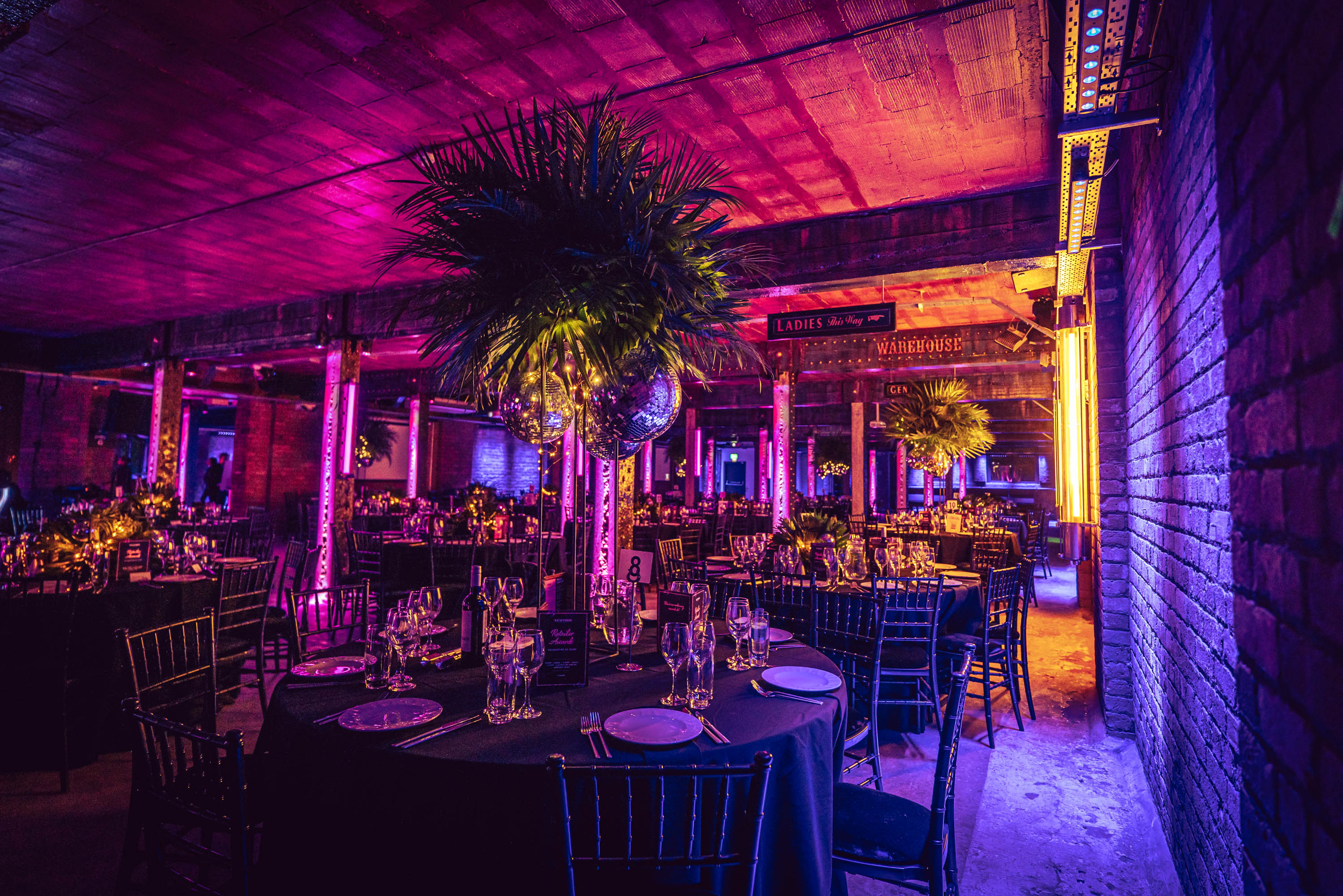 Elegant event space at Tobacco Stores with round tables, purple lighting, and lush greenery.