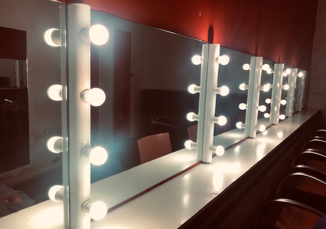 Vanity mirror setup with bright bulbs for pre-event grooming in Oxford House Theatre.