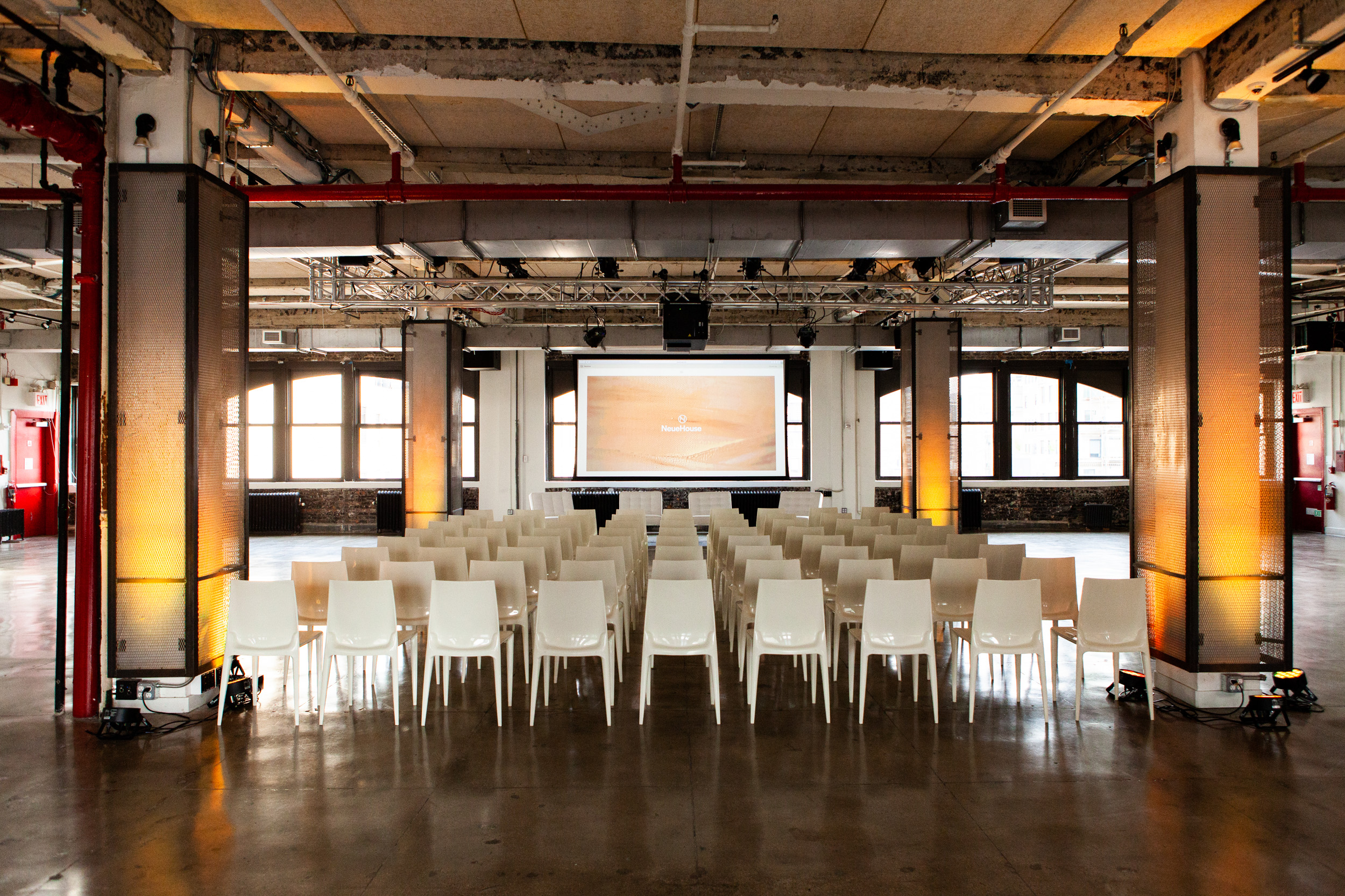 Modern event space in NeueHouse Madison Square with white chairs and large screen.
