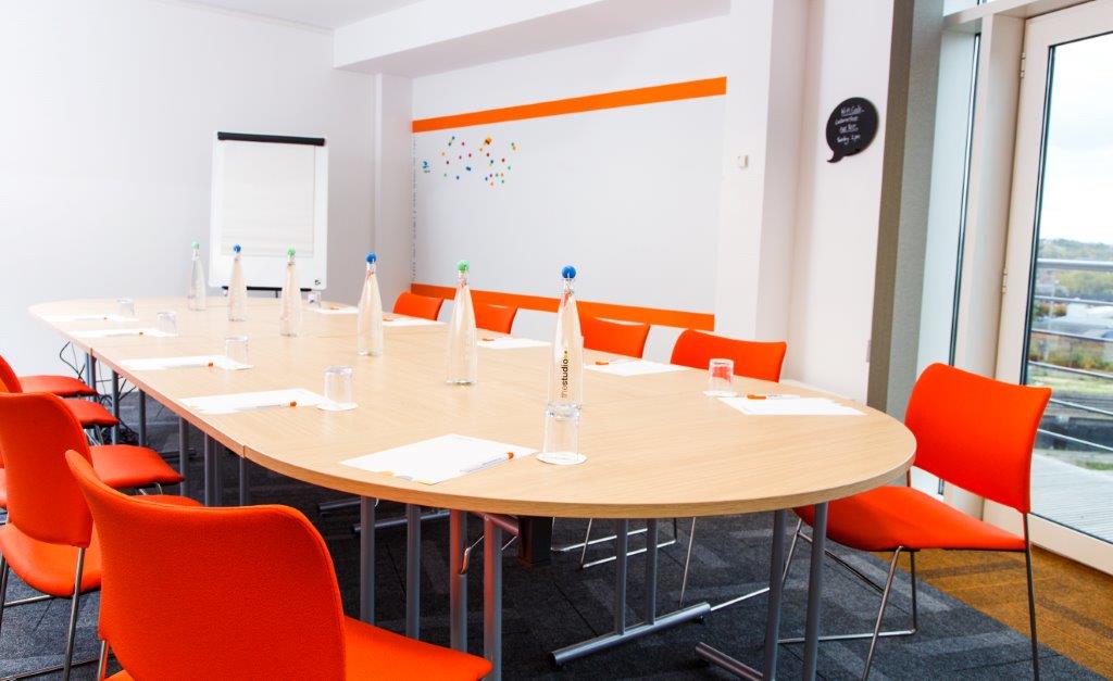 Modern meeting room in Leeds with oval table and orange chairs for collaborative sessions.