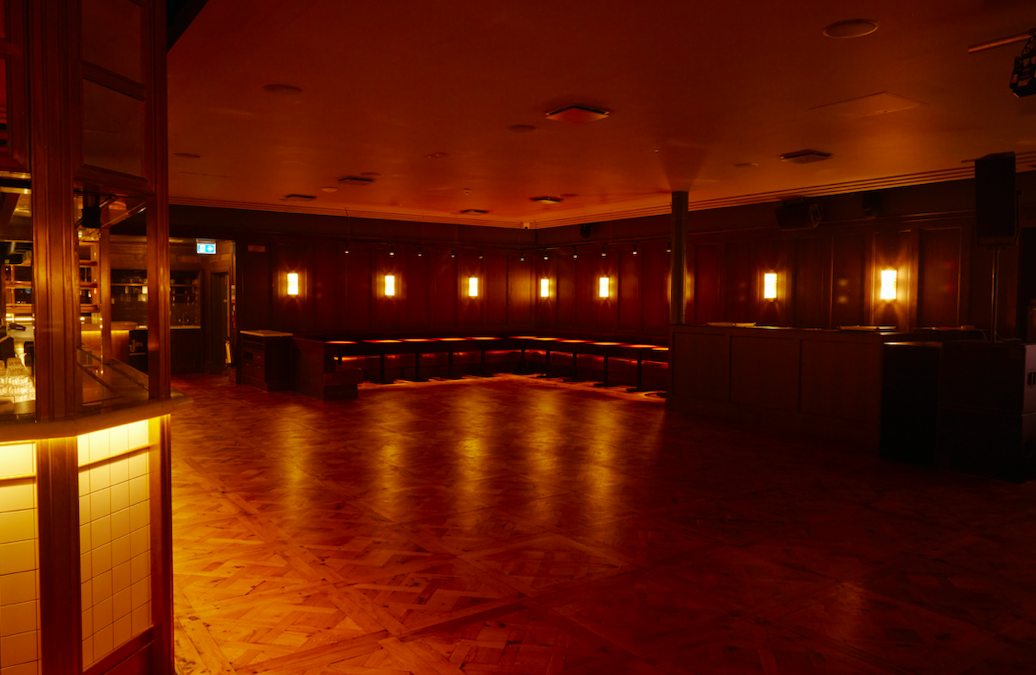 Alt text: "The Ballroom in NEON194, a warm-lit event space with polished wooden floor for gatherings."