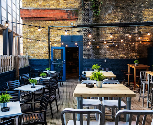 Stylish outdoor venue at Auberge London with wooden tables and string lights for events.