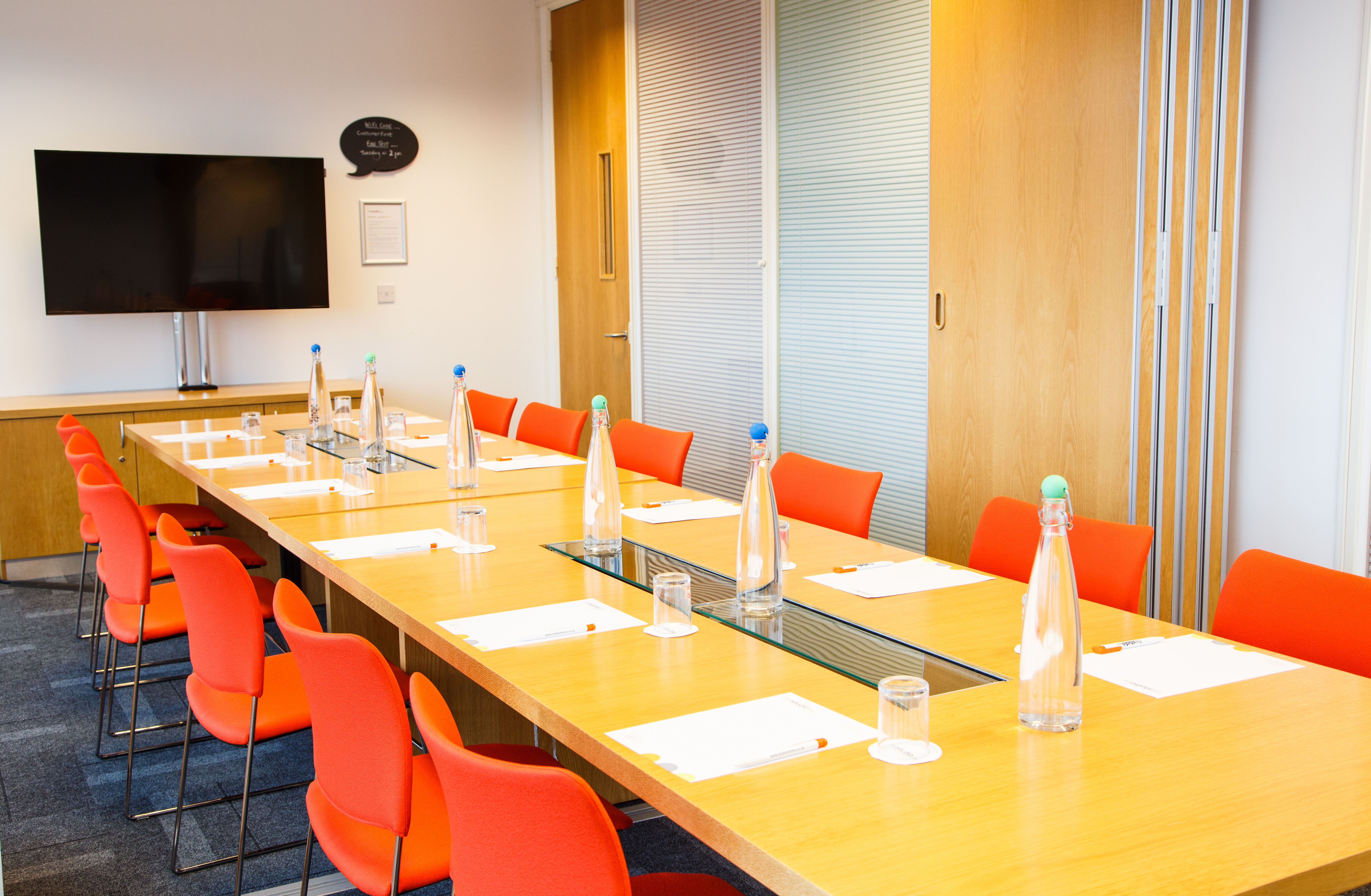 Meeting room in Leeds with wooden table, orange chairs for collaborative events.