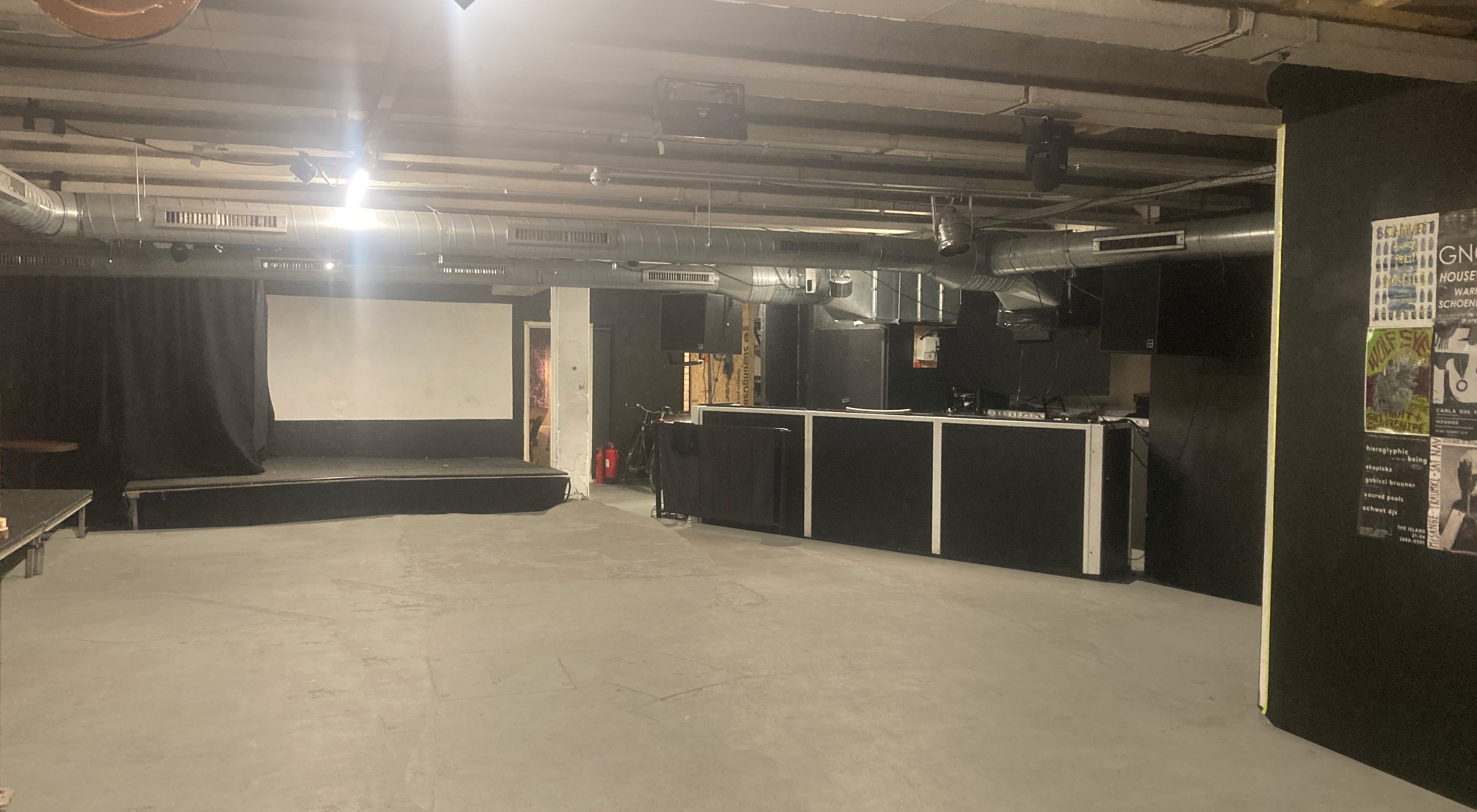 Versatile minimalist event space with stage and bar at Strange Brew for gatherings.