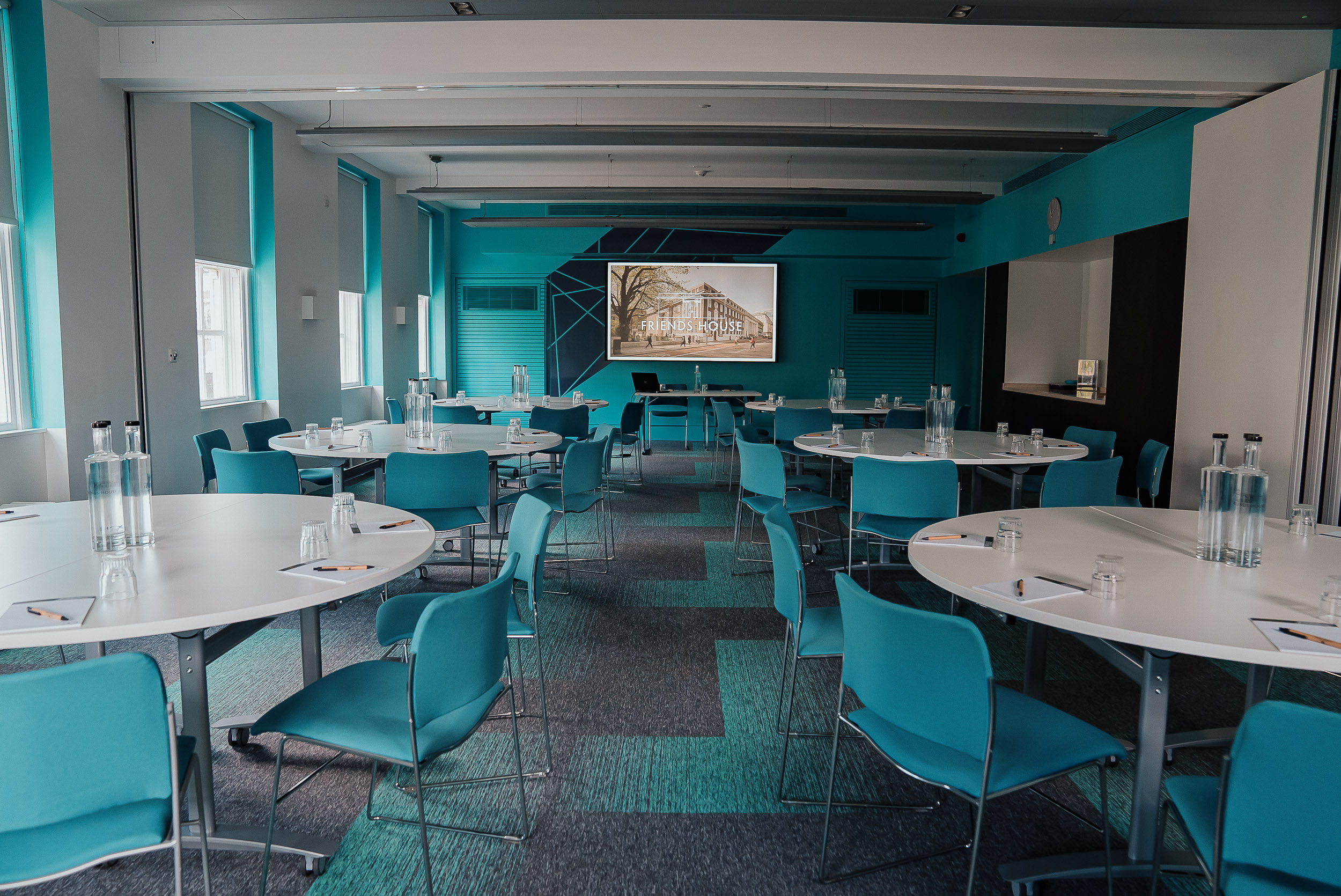 Modern meeting room with circular tables and turquoise accents for workshops and collaboration.