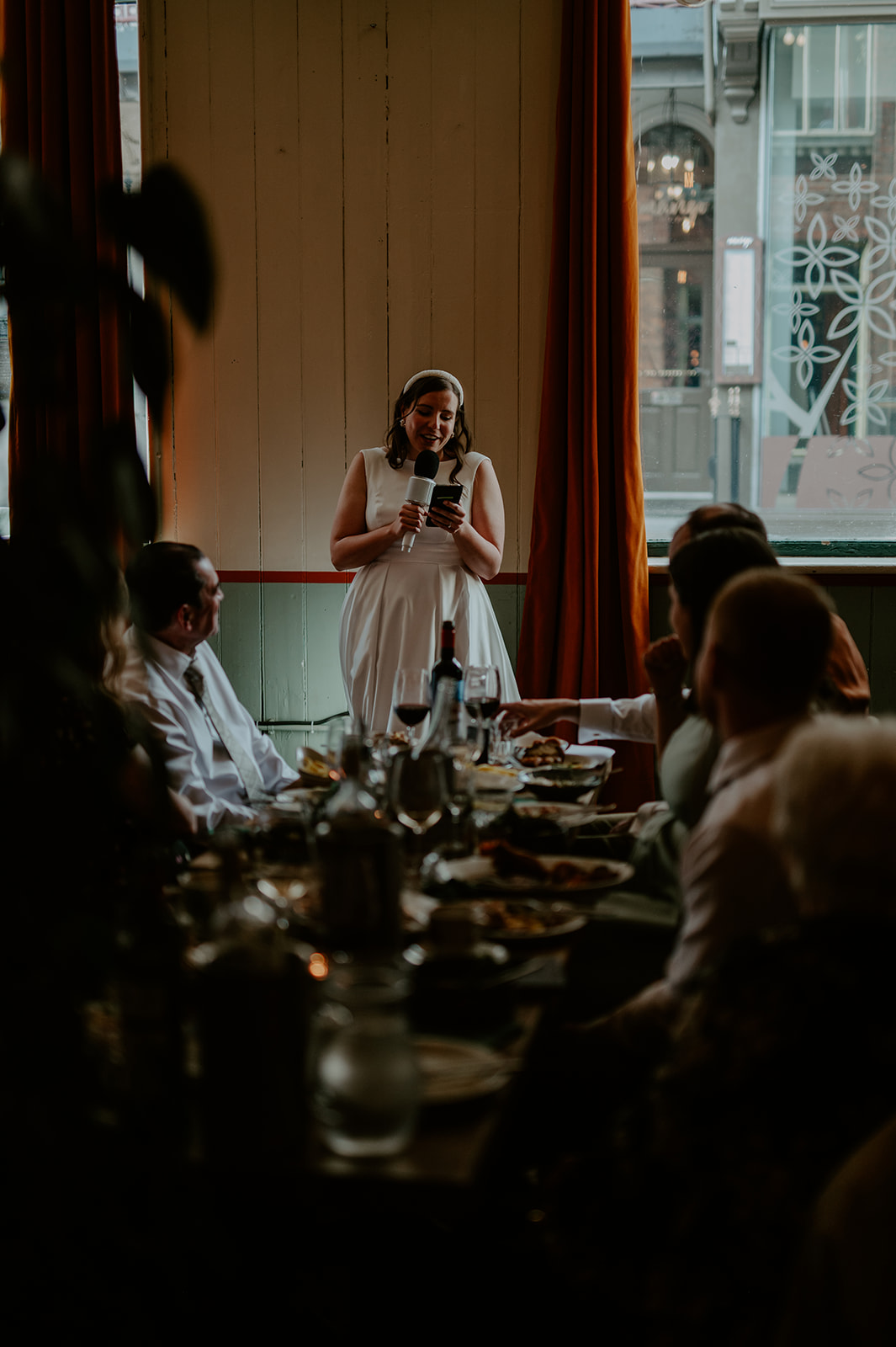 Woman delivering heartfelt speech at wedding reception in cozy, elegantly decorated venue.