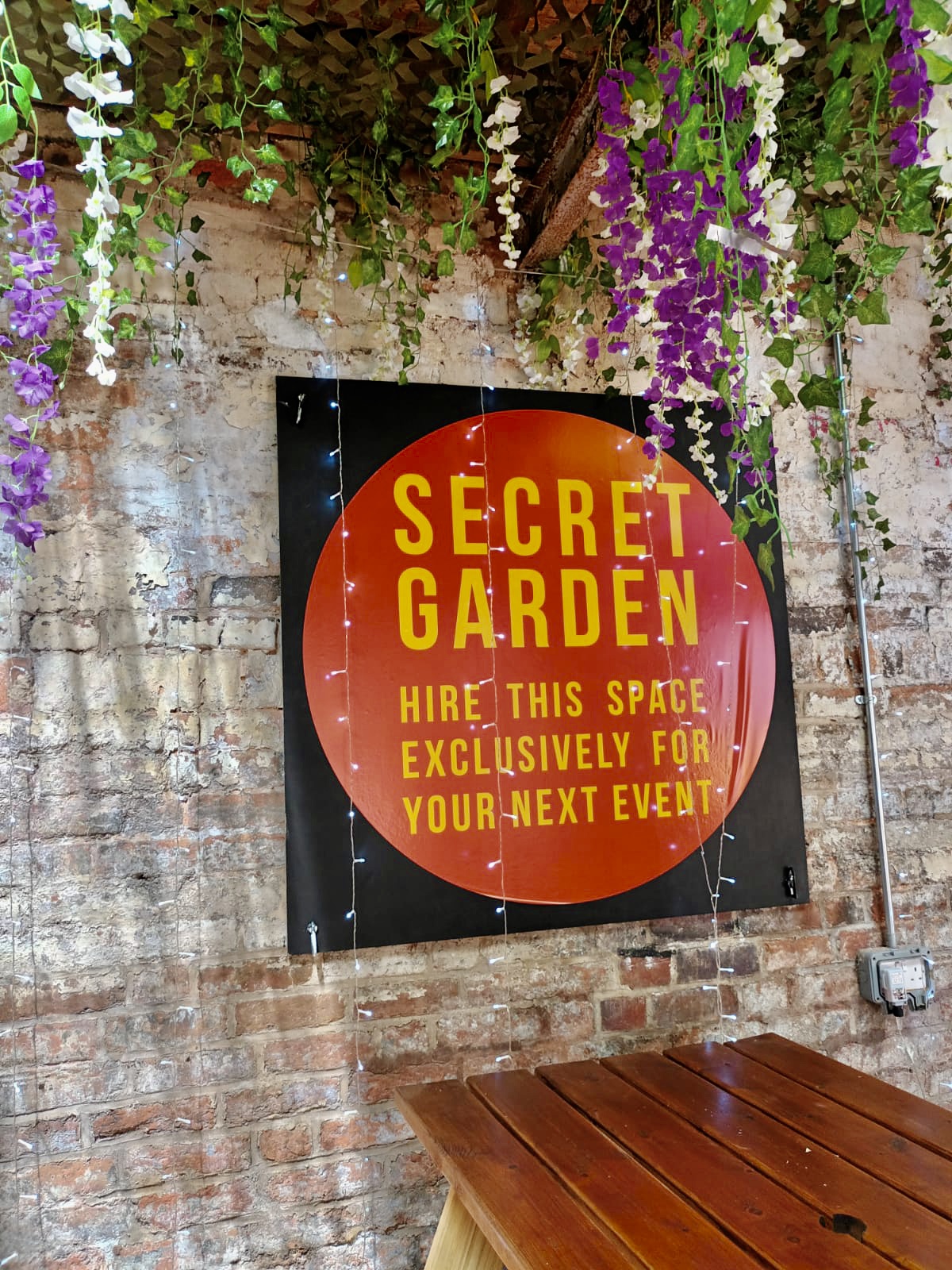 "Secret Garden venue sign with floral decor for exclusive events at The Button Factory."