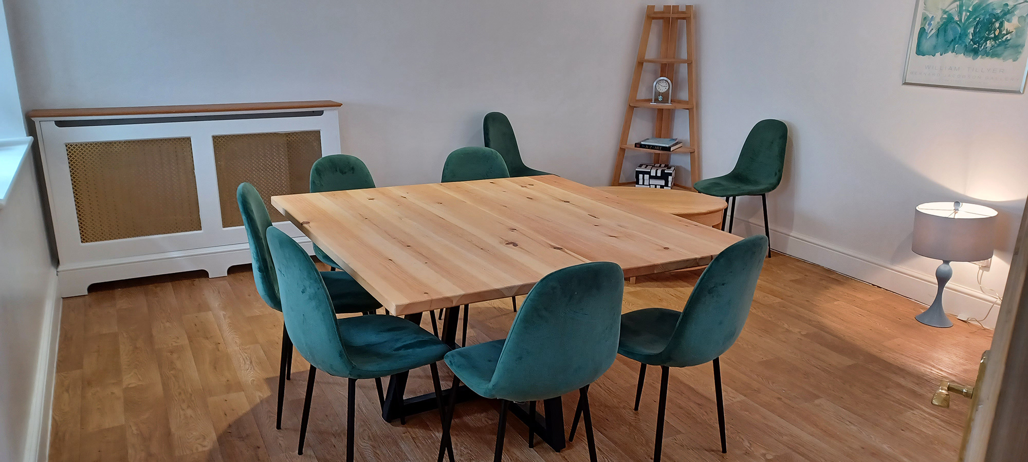 Modern meeting space at The George Cafe with large wooden table and plush green chairs.