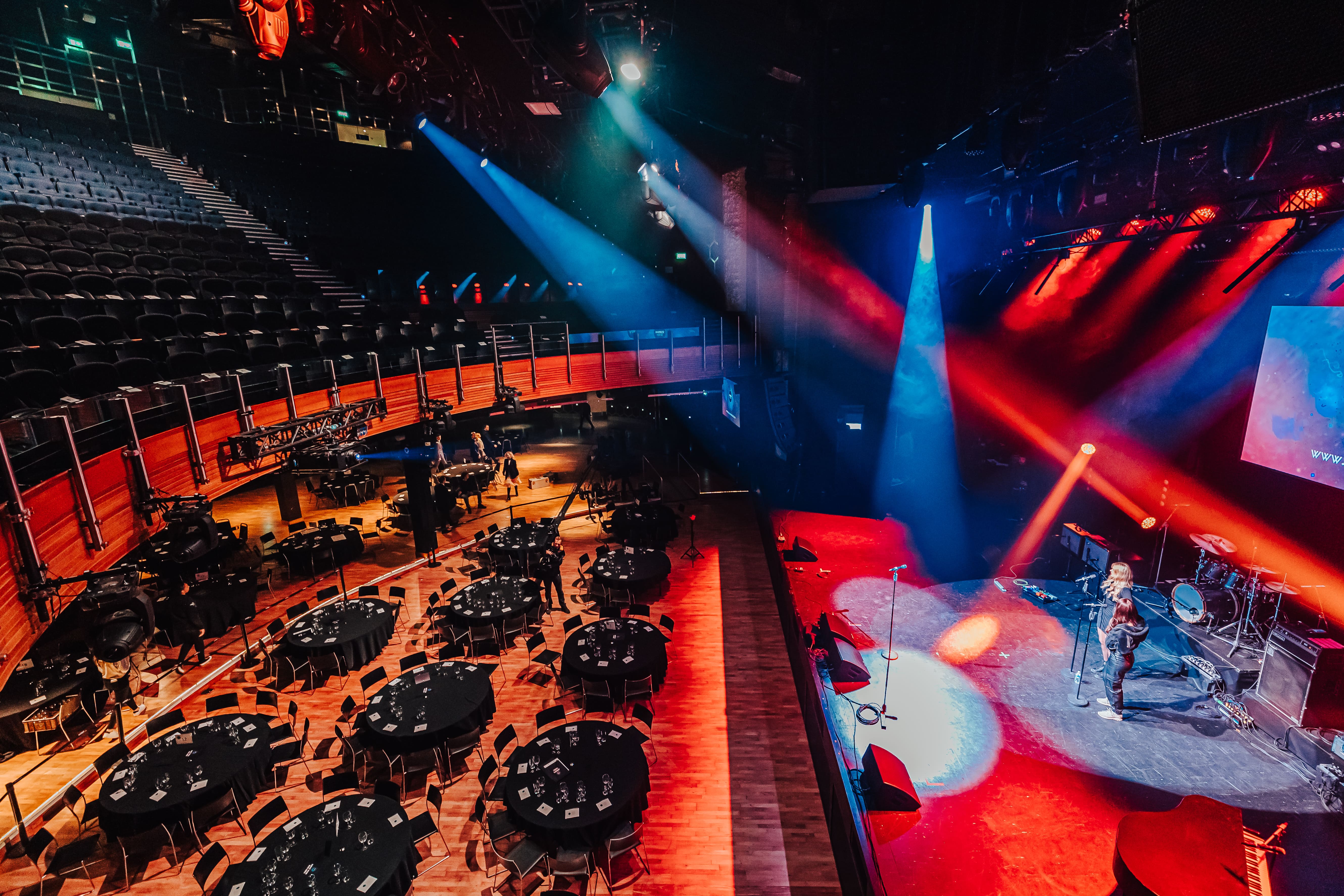 Main space at The O2, elegantly set for a gala with round tables and vibrant stage lighting.