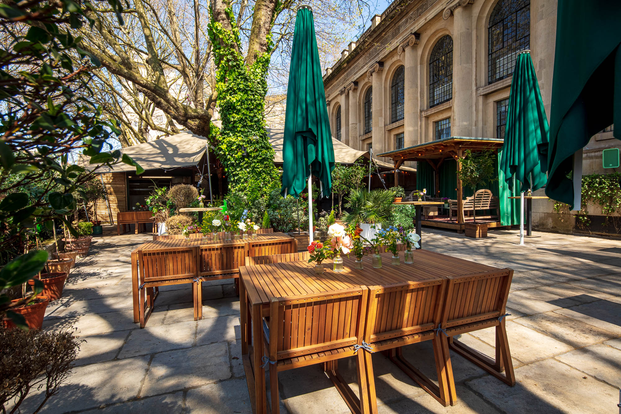 Outdoor event space at God's Garden, One Marylebone with wooden tables and green umbrellas.