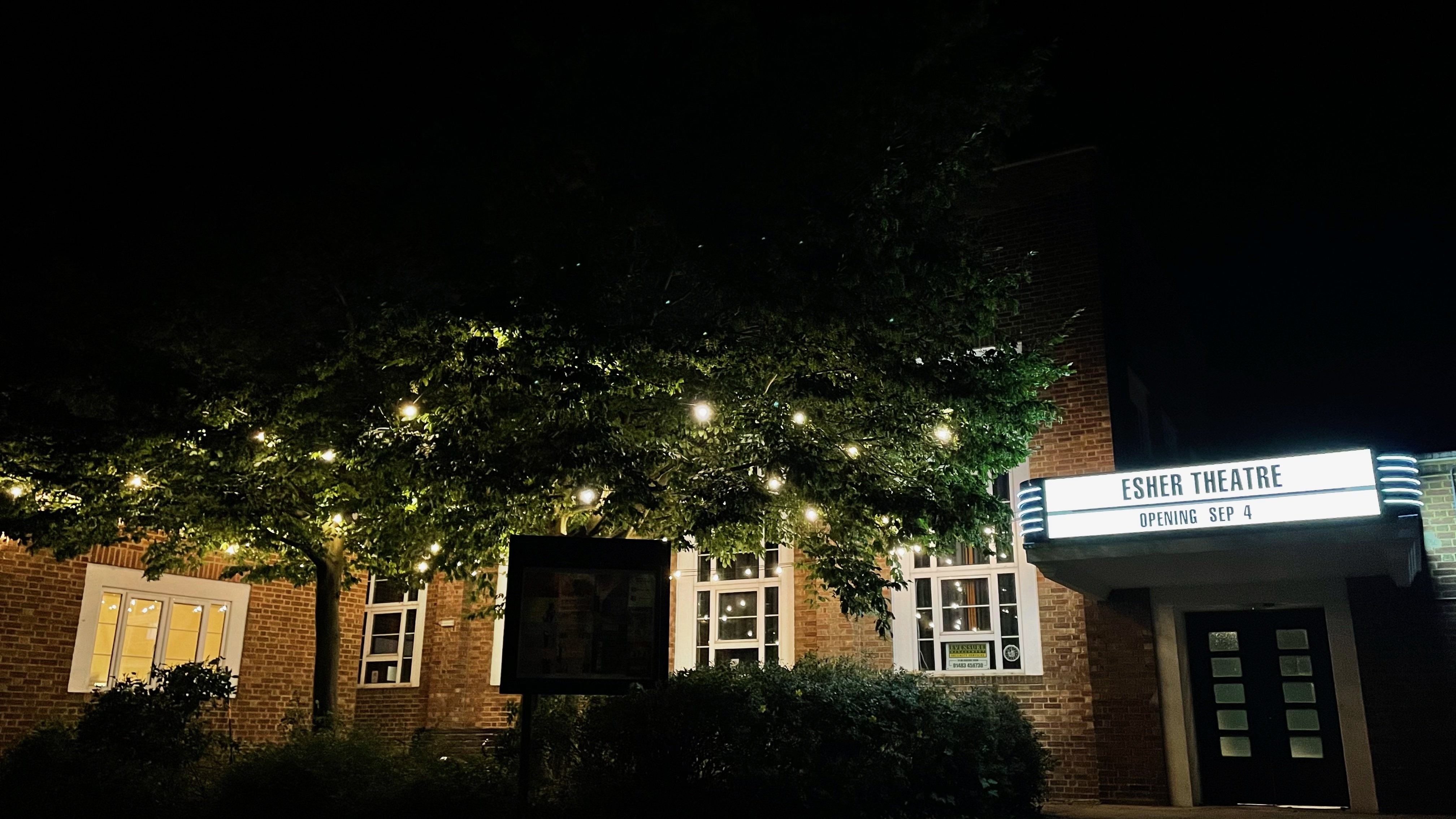 Esher Theatre at night, illuminated facade and marquee for events in a charming setting.