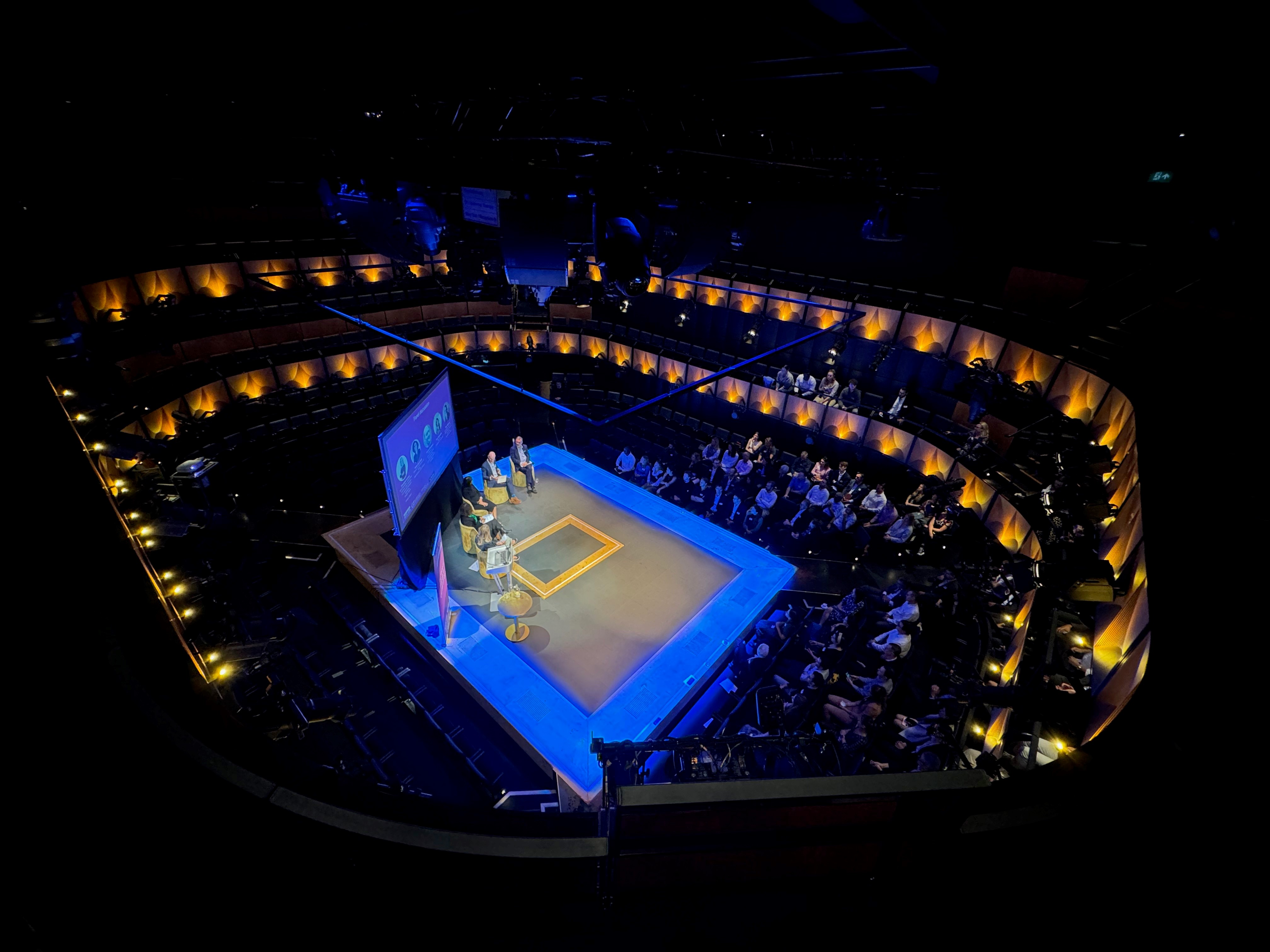 Auditorium in Sohoplace, London: blue-lit stage for panel discussion or keynote event.