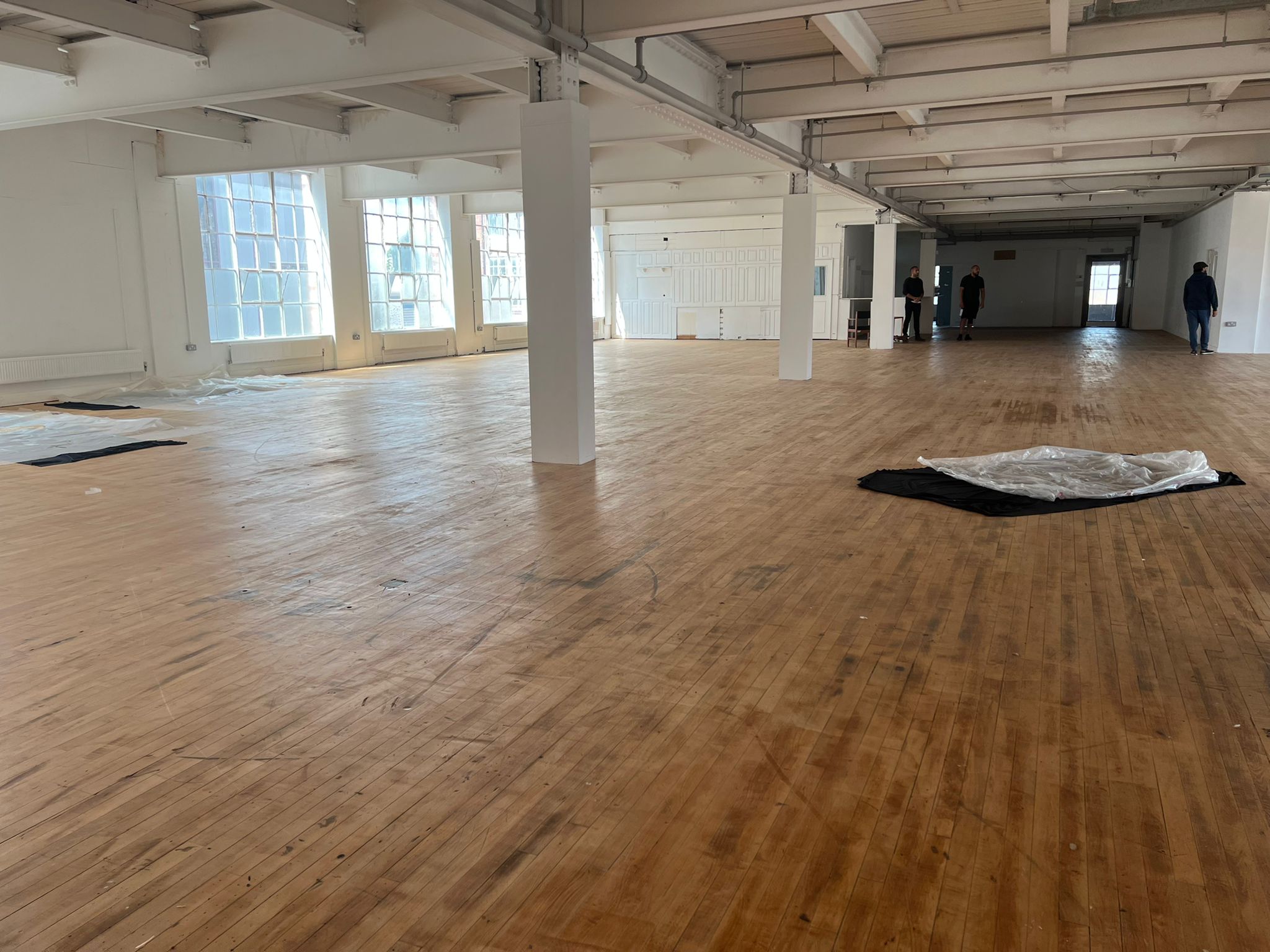 Spacious event venue with polished wooden floors and natural light, ideal for gatherings.