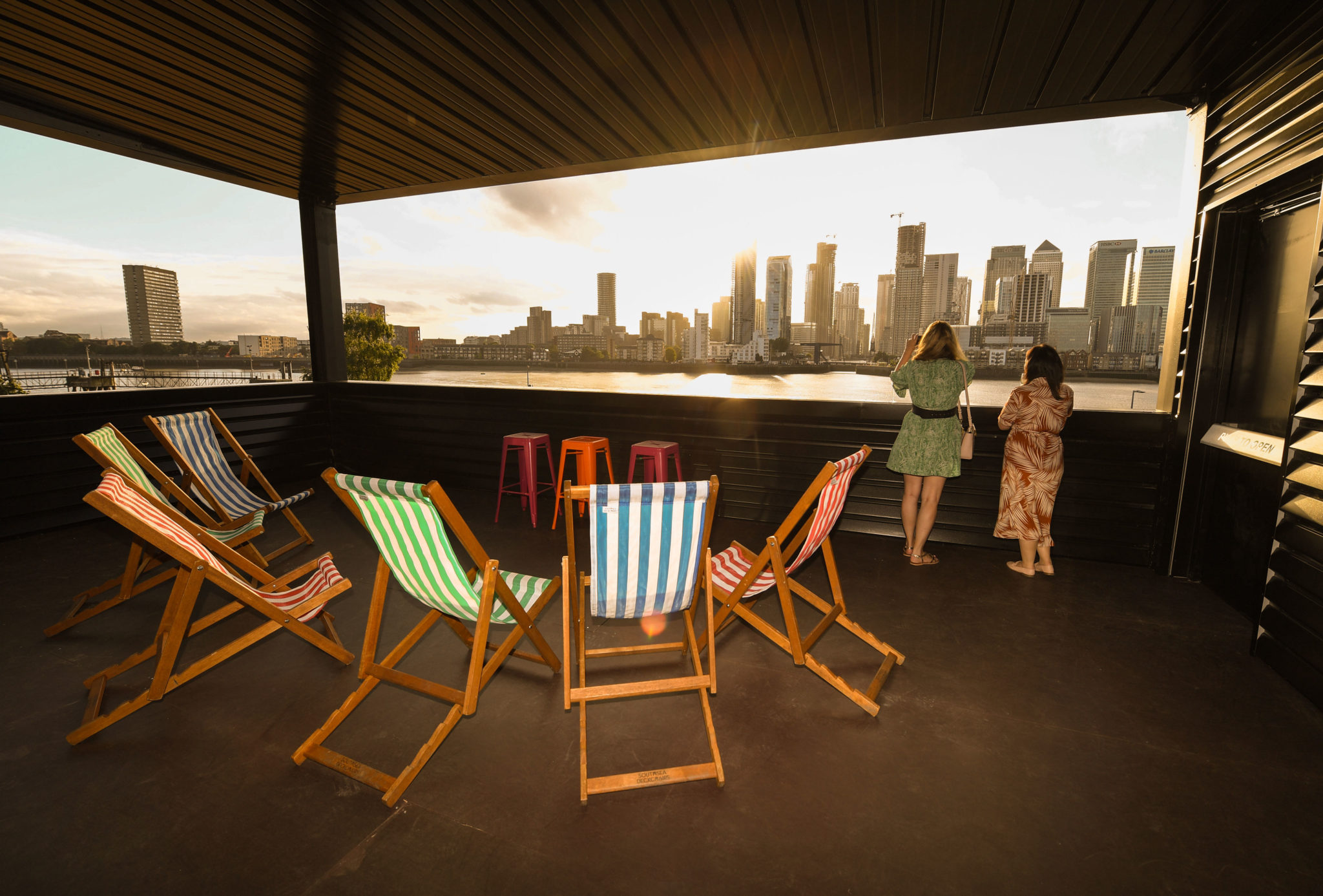 Stylish outdoor summer party venue with colorful deck chairs and city skyline at sunset.