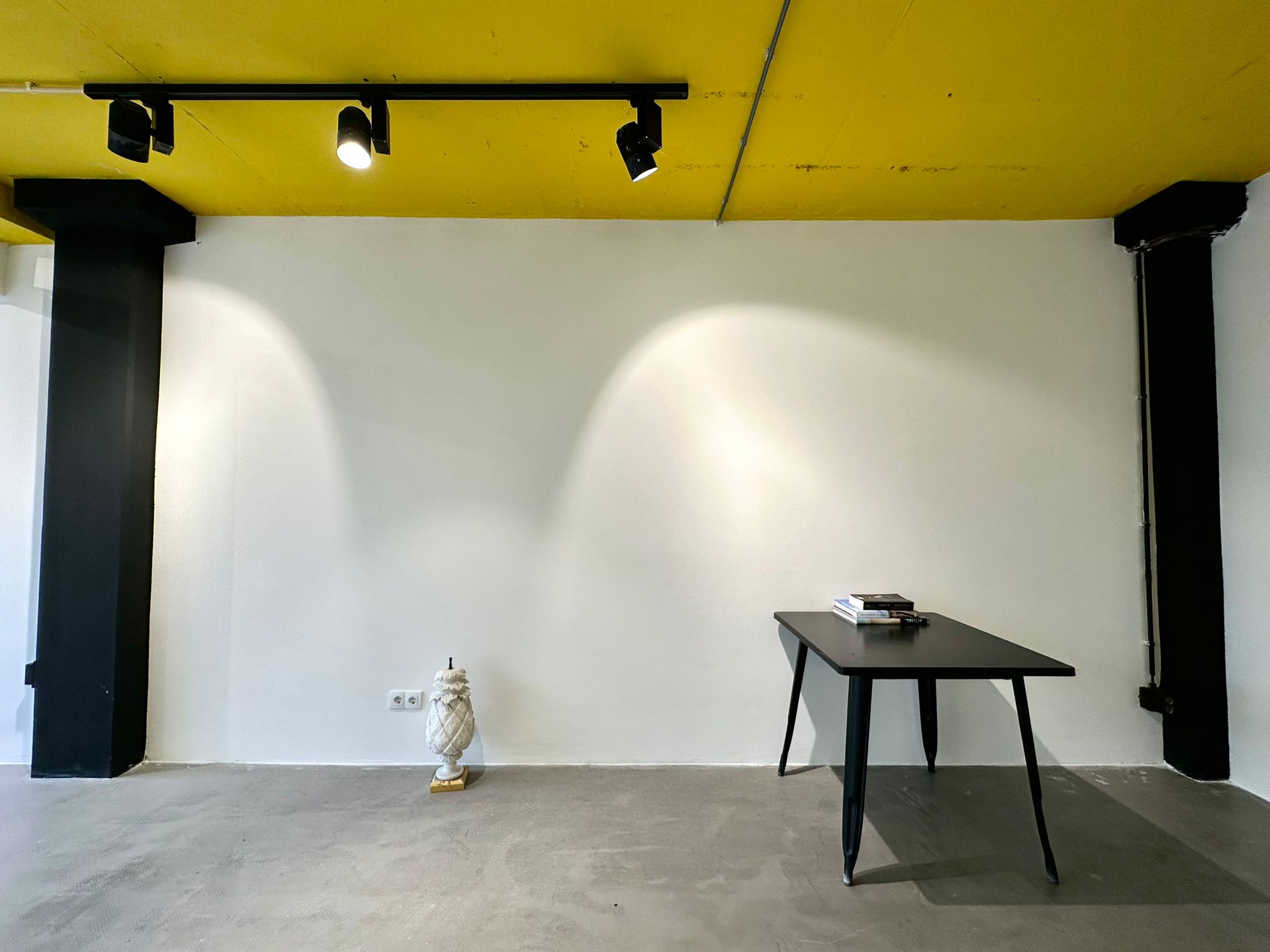 Minimalist urban hotel event space with sleek black table and yellow ceiling.