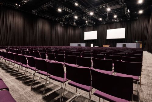 Spacious ICC Belfast conference venue with empty chairs and large screens for events.