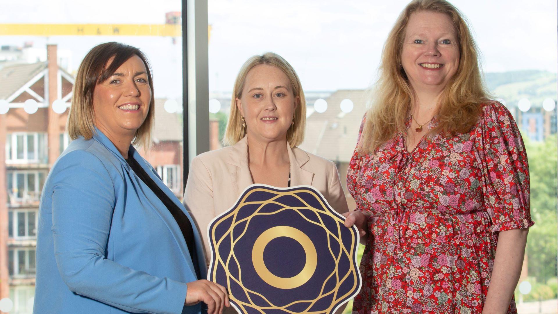 Professionals holding emblem in bright ICC Belfast River Rooms, showcasing event collaboration.
