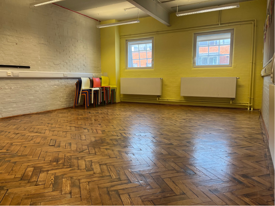 Versatile rehearsal room with wooden floor and bright yellow walls for workshops.