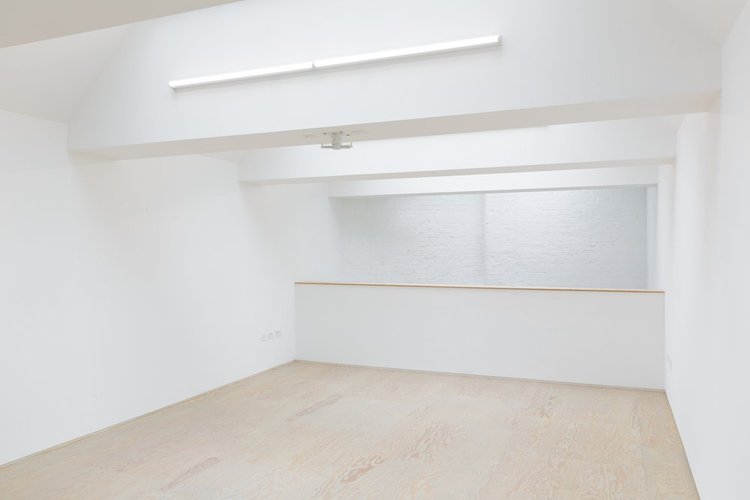 Minimalist event space with white walls and wooden floor, ideal for meetings and workshops.
