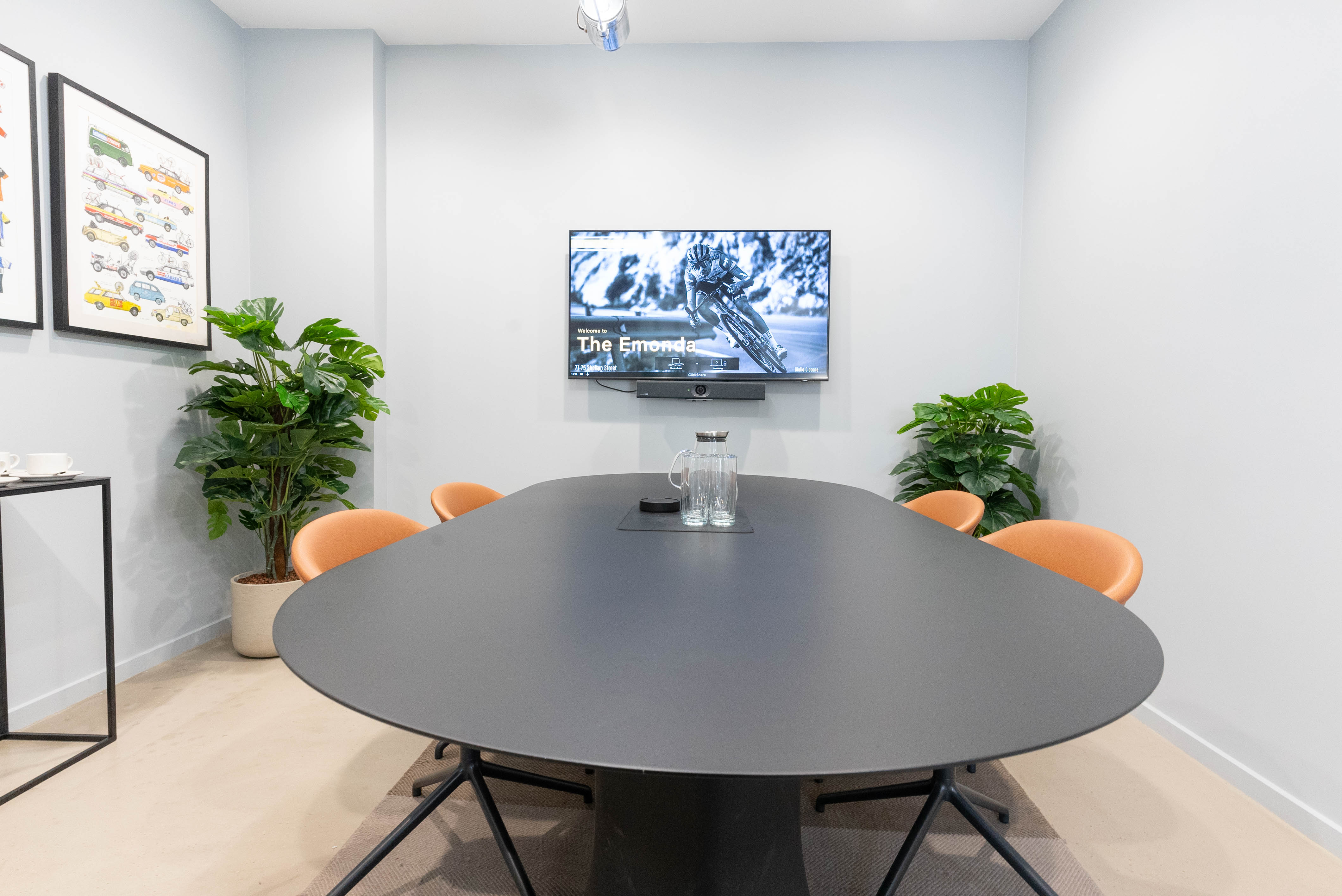 Modern meeting room with oval table, large screen, and greenery for collaborative events.