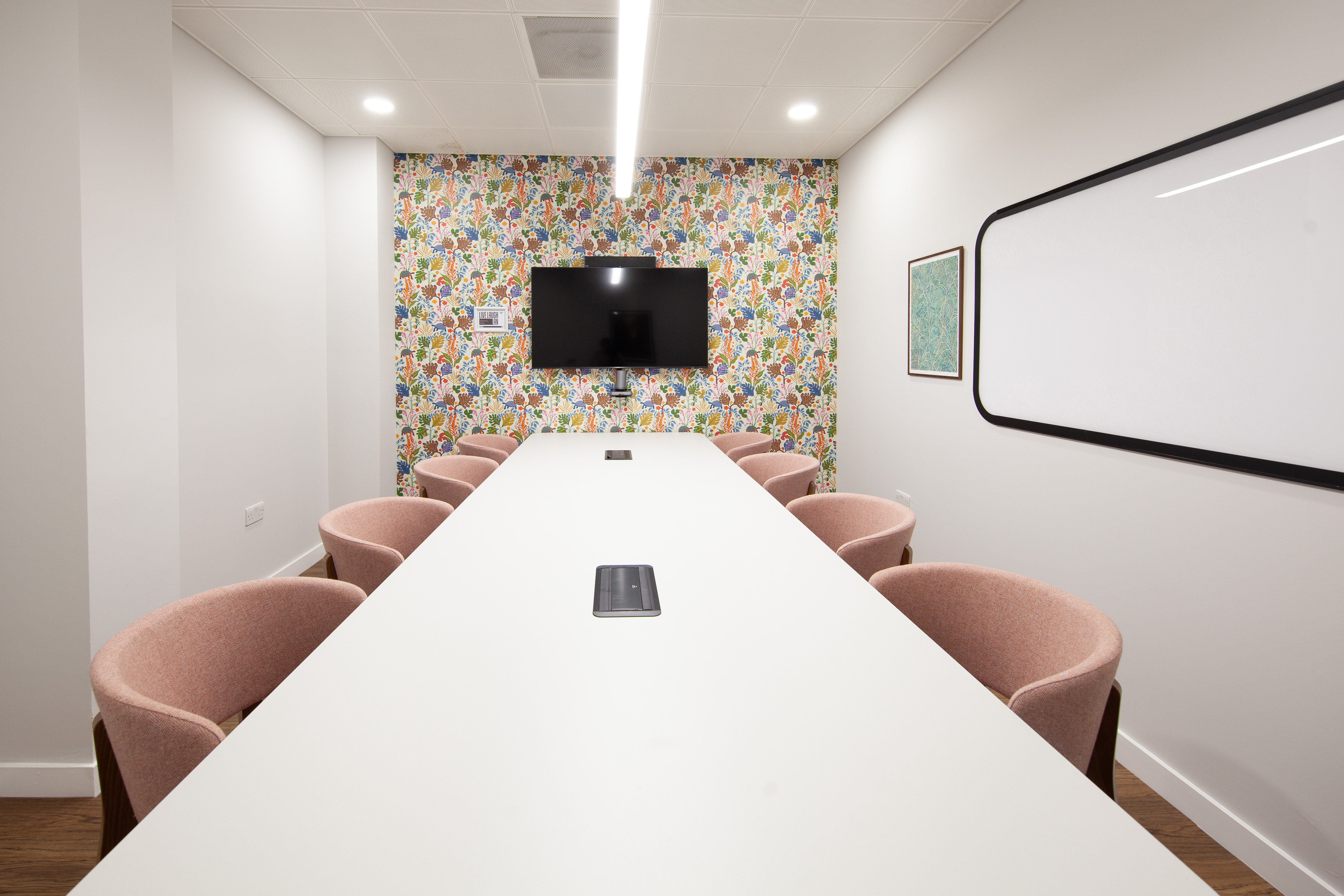 Modern meeting room with white table and pink chairs, ideal for team brainstorming sessions.